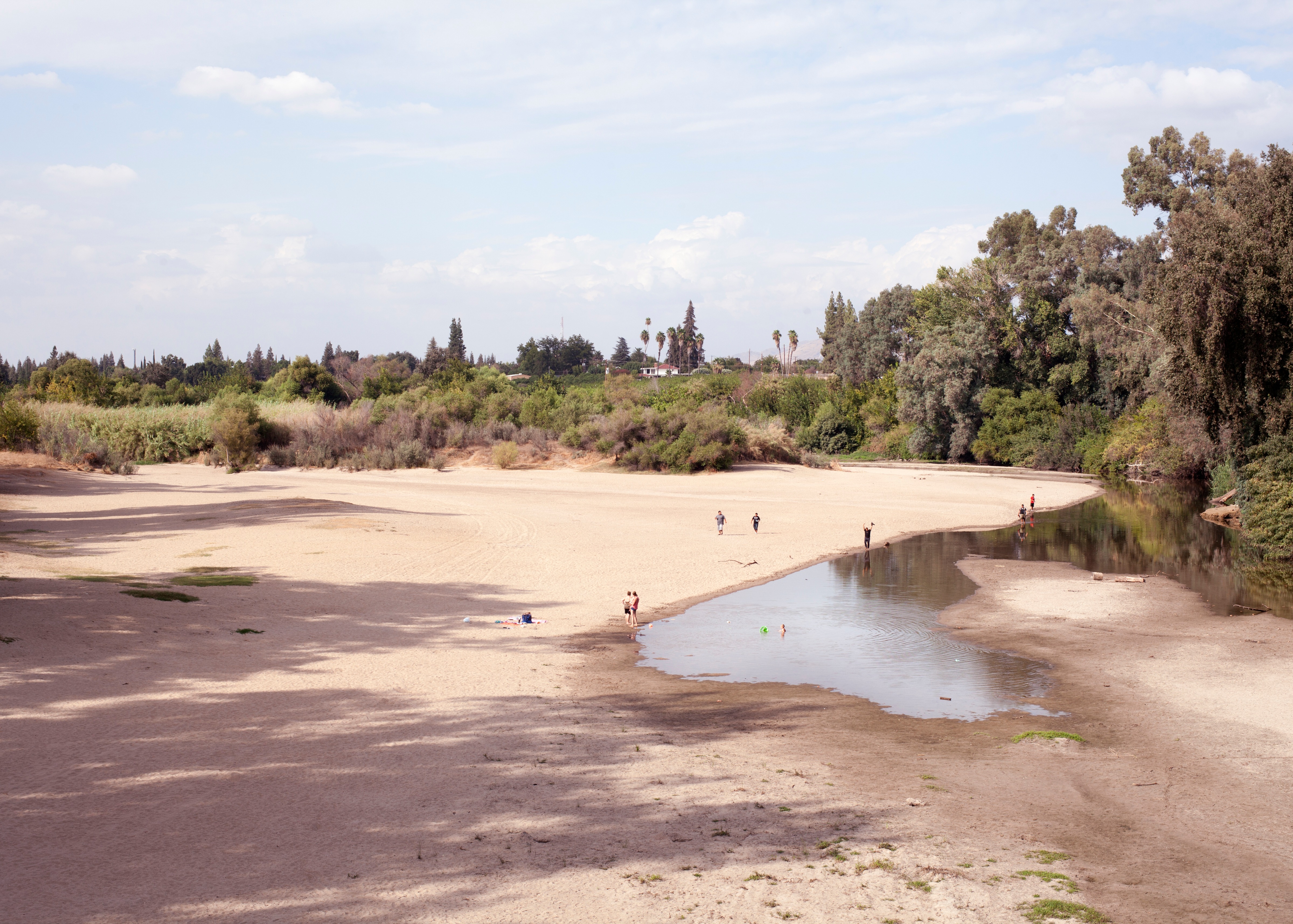 A photograph of a nearly dried riverbed, with several people standing at various spots along its edge.