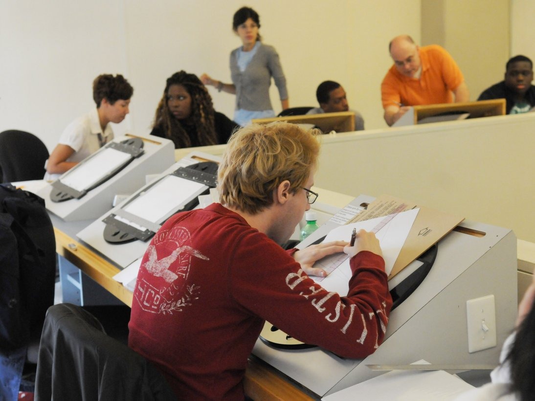 A diverse group of students draw with animation tools inside a studio while faculty members supervise.