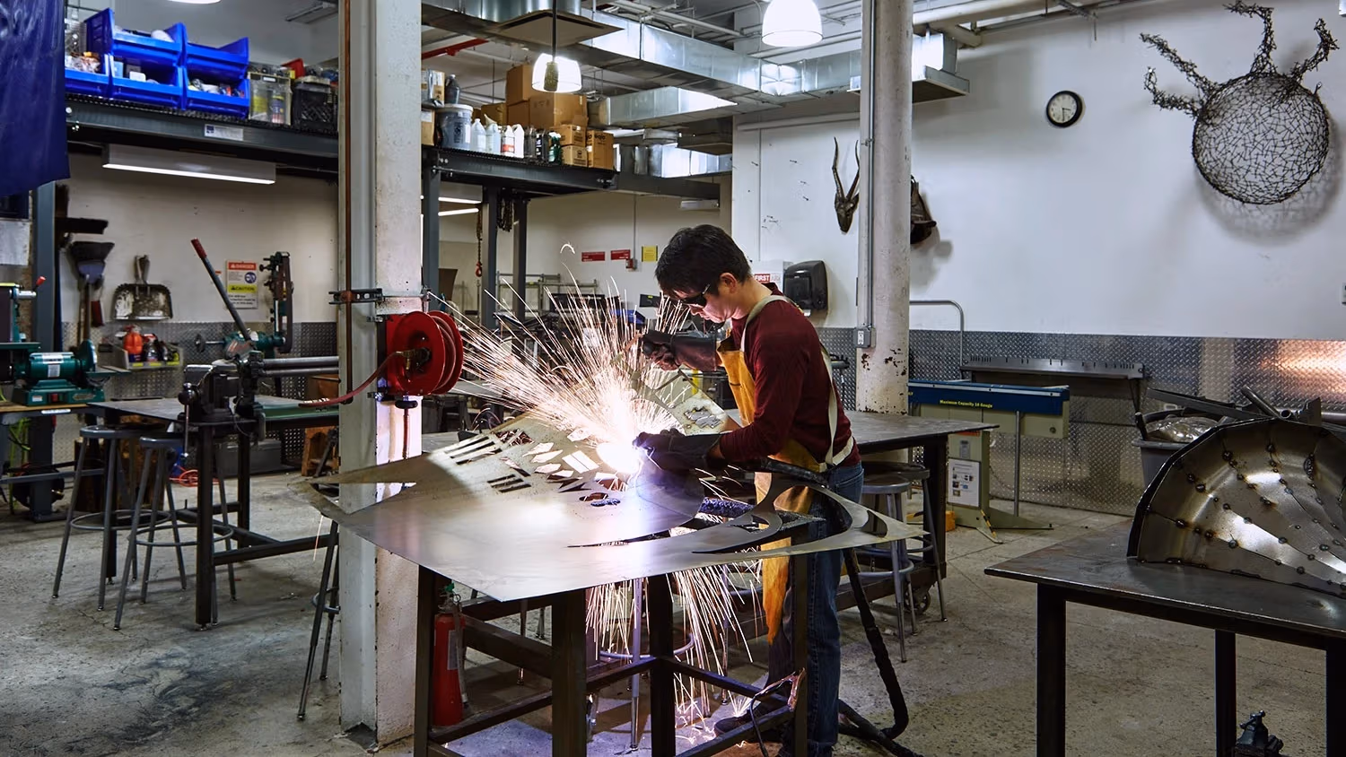 Student wearing protective goggles while metalsmithing; sparks are flying everywhere