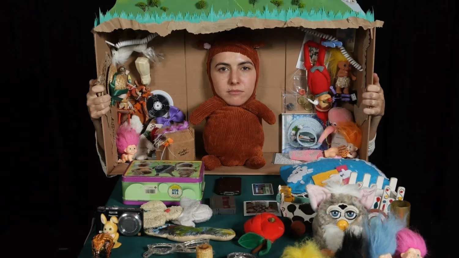 Face of Shayna Strype on teddy bear body in tableau with cardboard box and toys