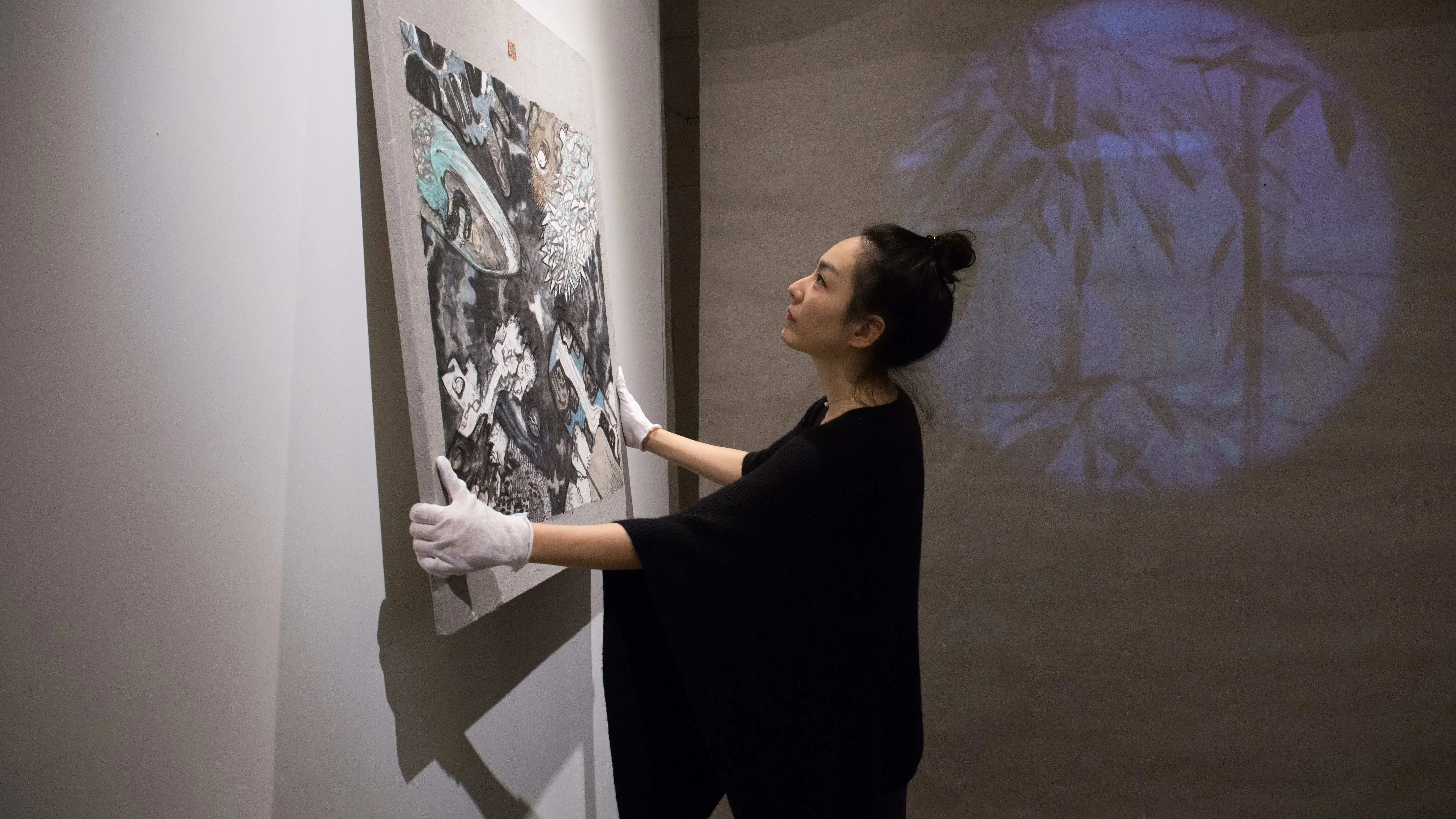 a person hanging a painting up on a white wall wearing white gloves with a dark curtain in the background