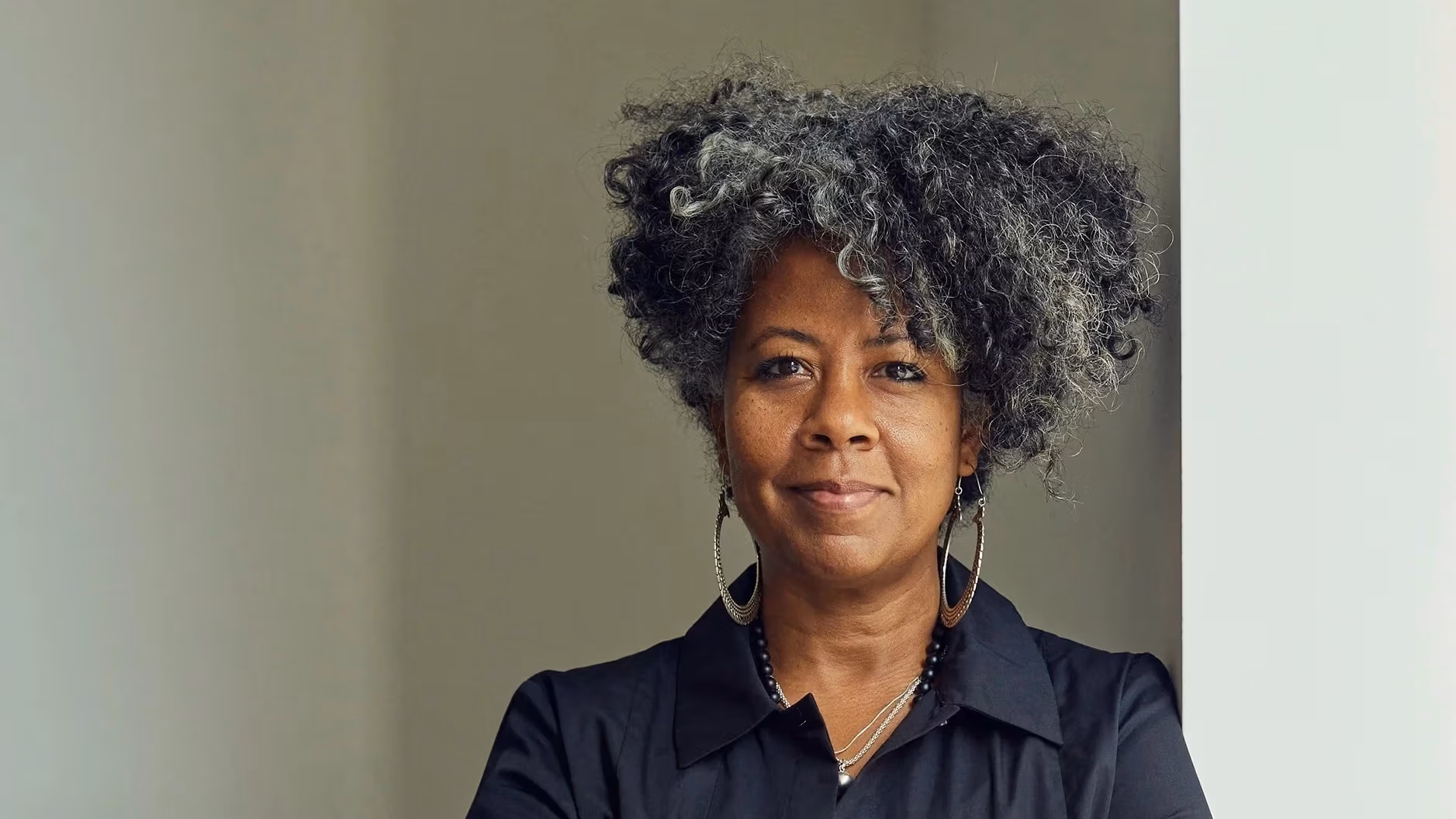 Portrait of the artist Torkwase Dyson smiling and leaning against a wall with arms crossed.