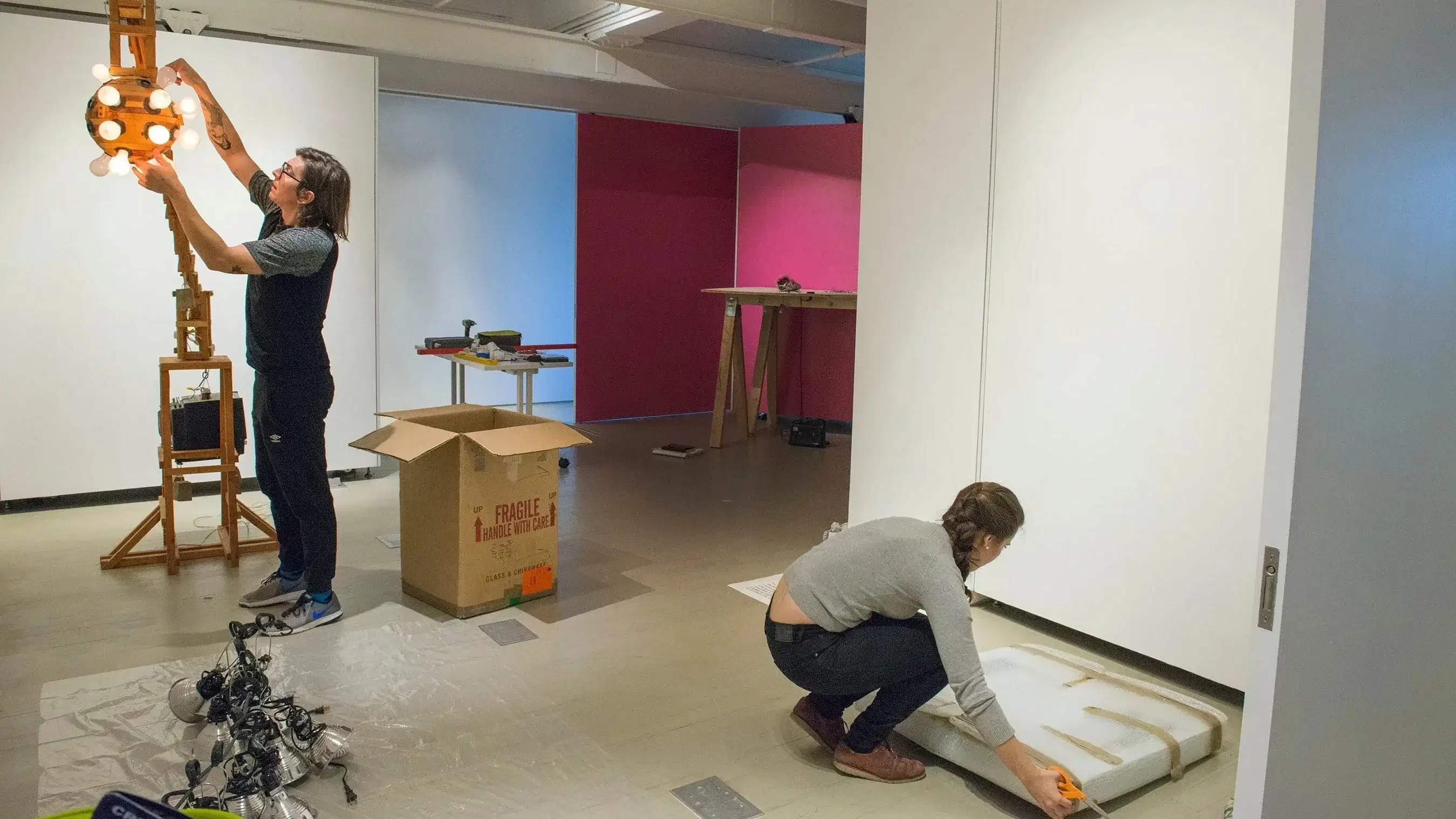 Two students unpacking and hanging artwork in a gallery space 