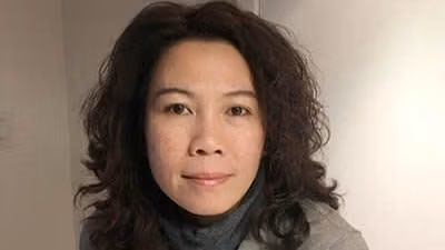 A headshot-style photograph of a person posed in a room with blank walls.