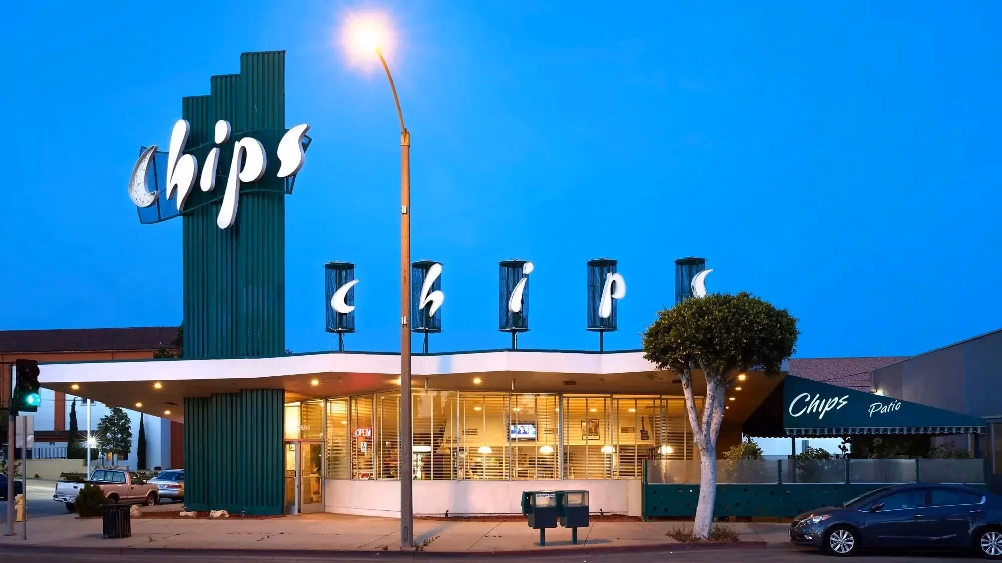 A photograph of the exterior of the Chips Restaurant in Los Angeles, CA, which features a tall, dark green column that bears the name of the restaurant in white letters, and a single story dinning room. 