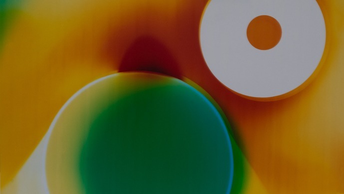 Three circular shapes lined up diagonally from left to right, bottom to top. The top right one has an orange circle in the center, the middle one a green and yellow hue and the bottom left one has a blue ring within. There are green, orange, yellow red and blue tones dispersed throughout the image. 