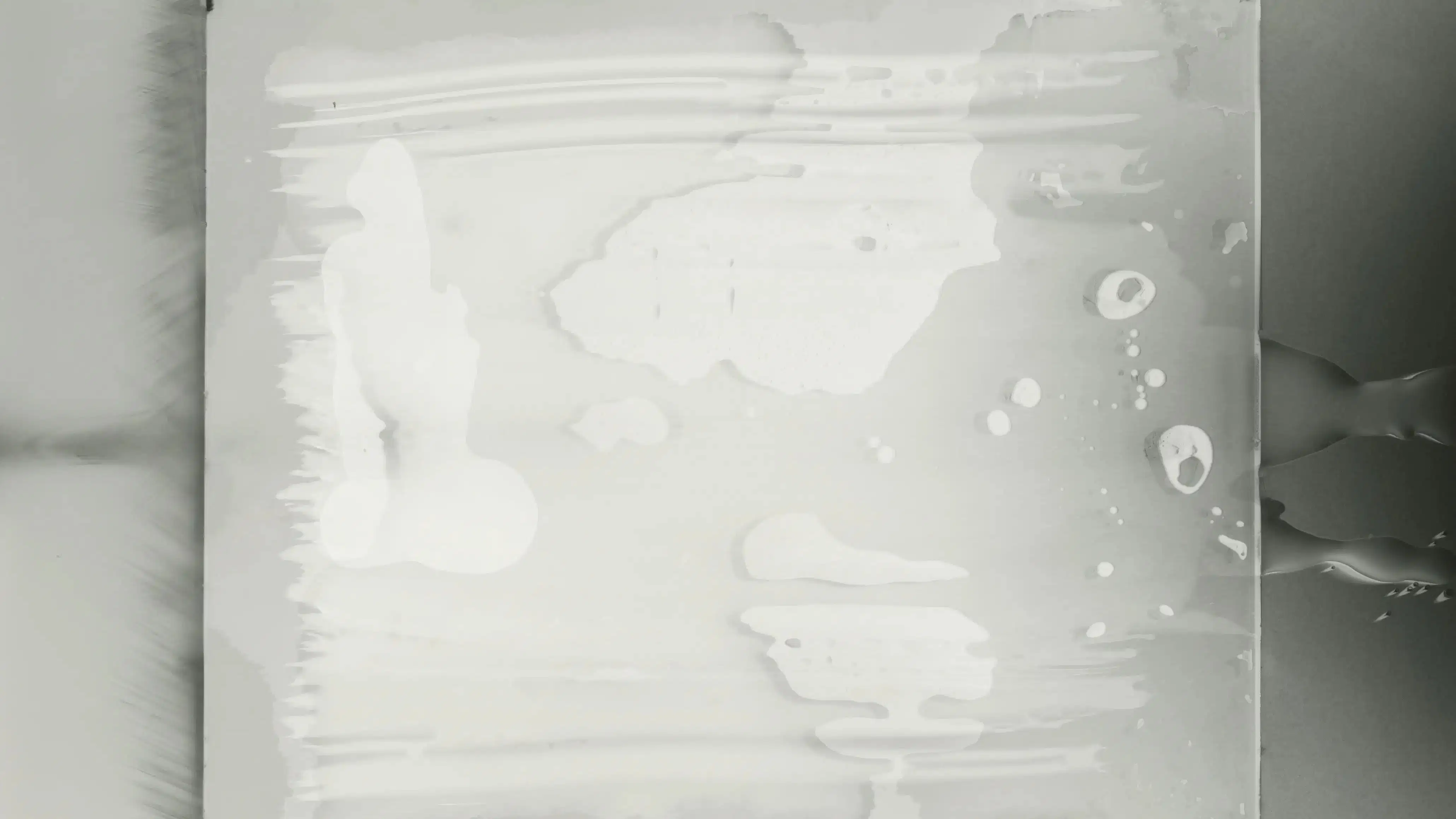 A whiteish paste-like fluid appears pressed between a background and a pane of glass, with bubbles and freeform shapes appearing in and extruding from the glass.