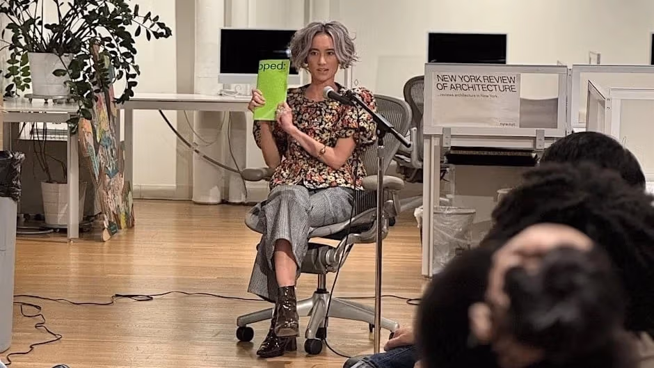 a person with gray hair holds up a book in front of a room of event attendees