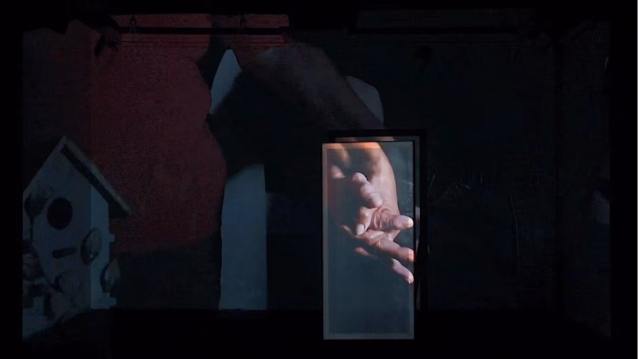 A red room with a black and white painting of a house and more. There is a video being screened in the room on a panel.