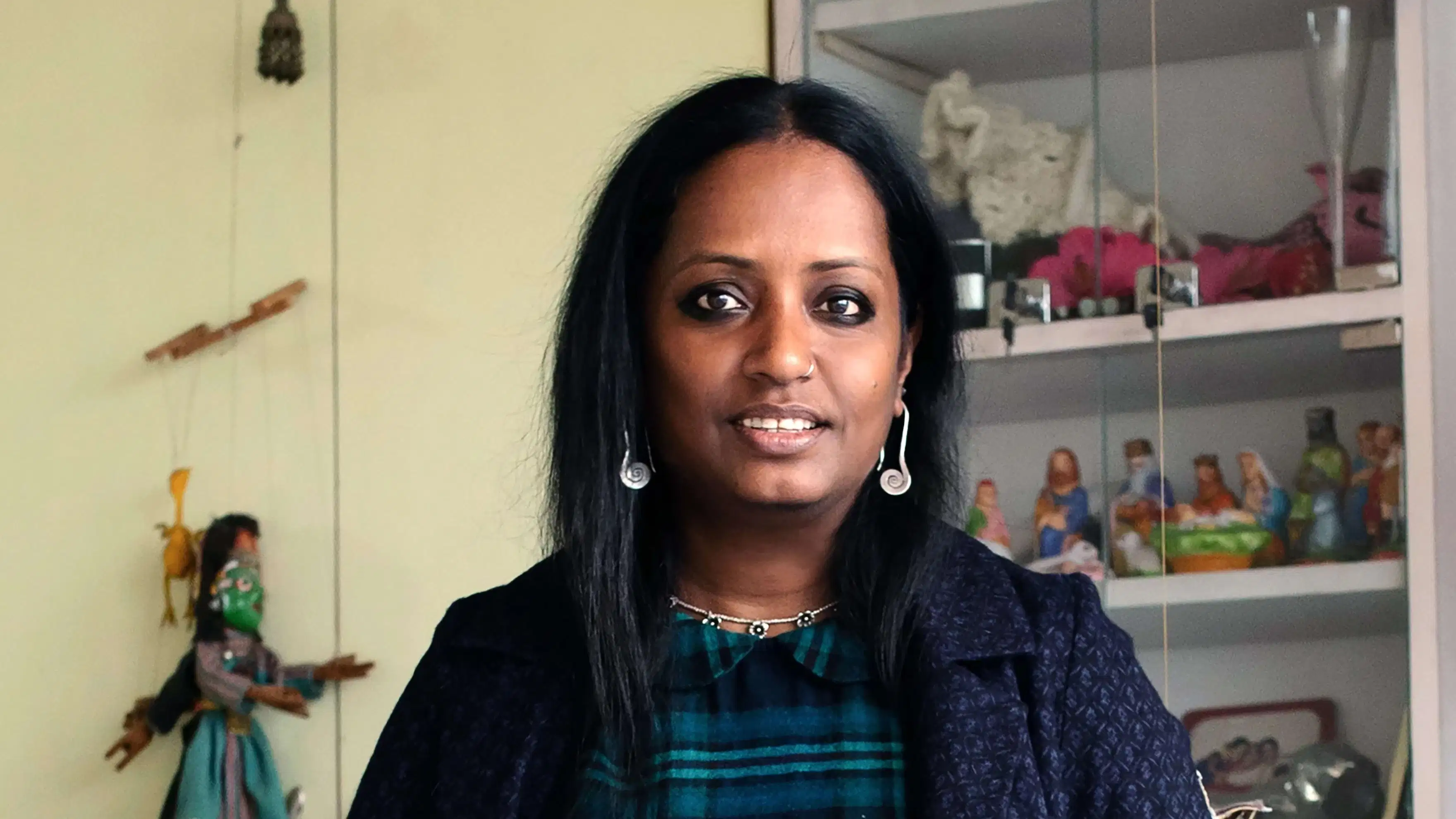 A photograph of Mithu Sen. Mithu is standing int he center of the photo and is wearing a blue and green plaid shirt with a davy blue jacket.