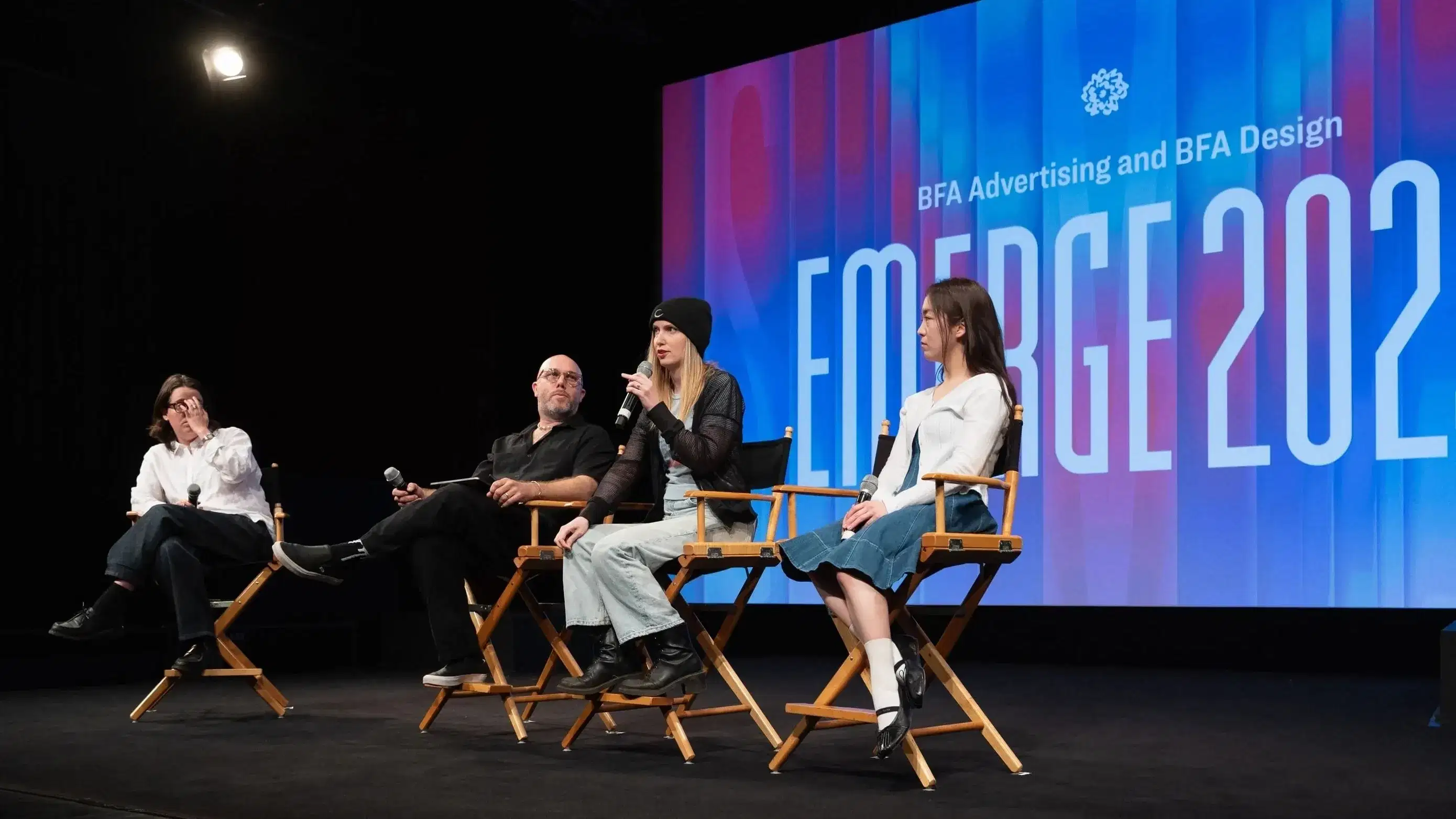 a group of people sit on a stage in front of a screen that reads "EMERGE"