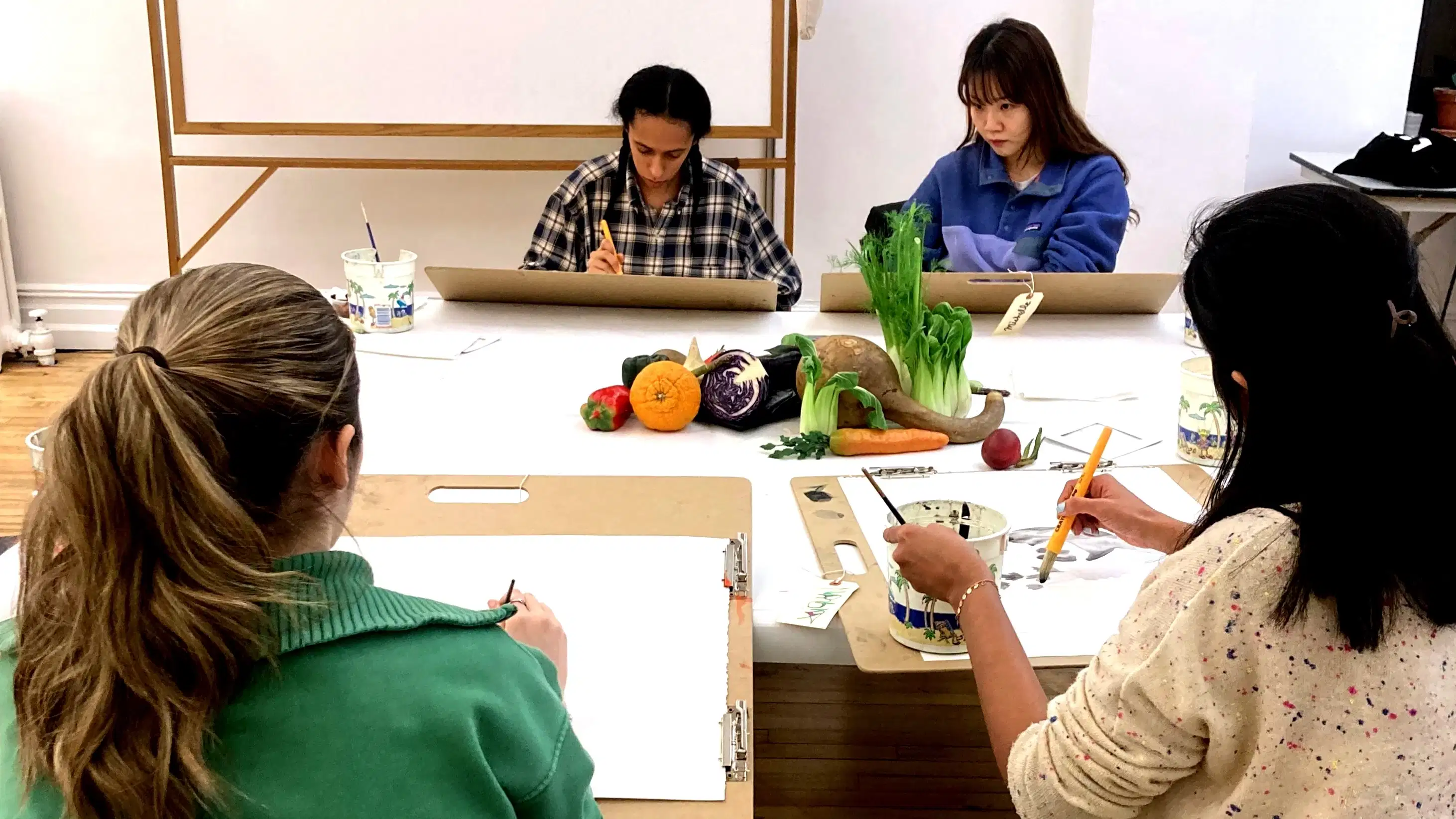 Photograph of four students drawing a still life of various fruit