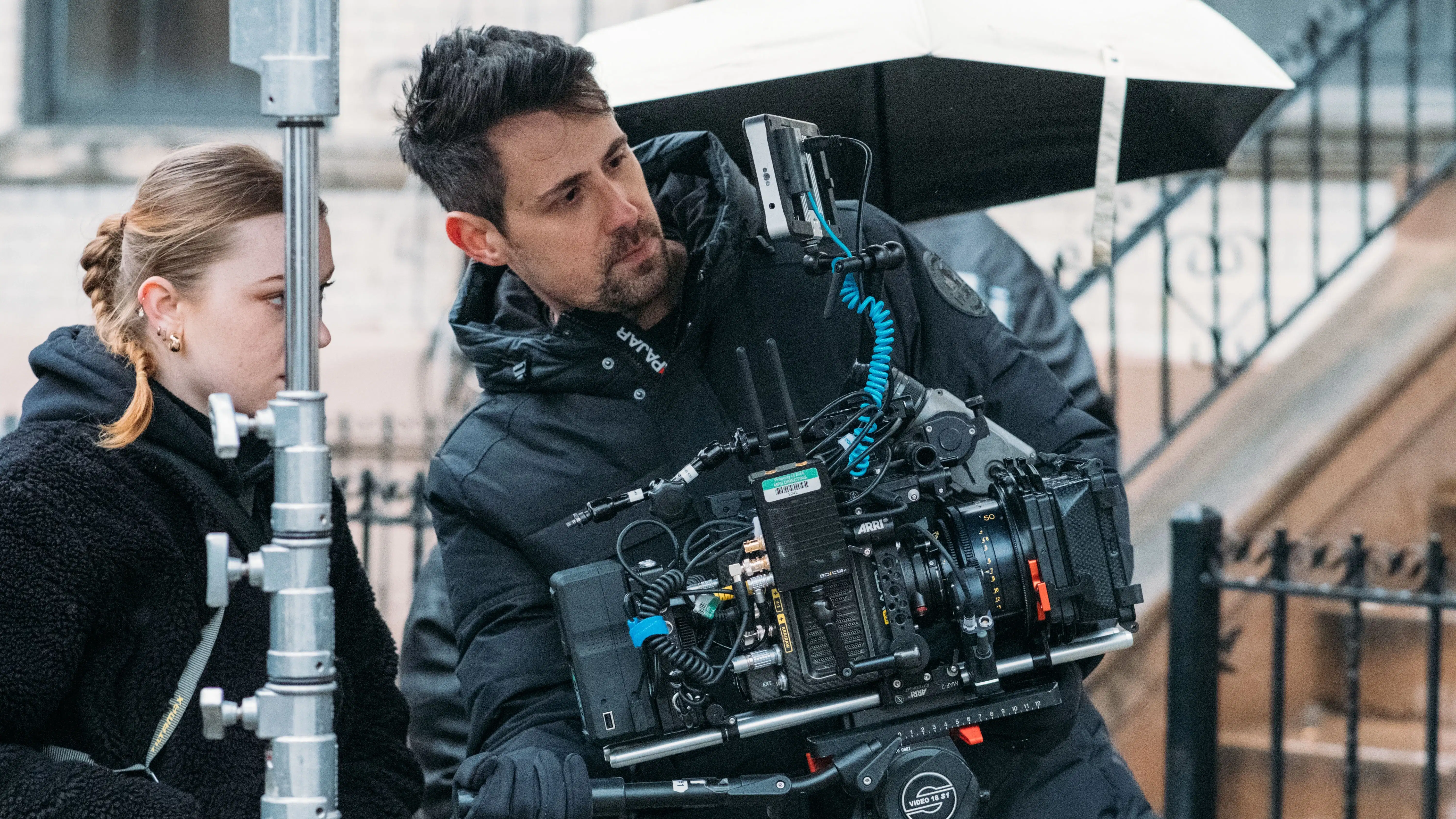 Photograph of two people, a cameraman holding a sophisticated digital film camera, the other directing the cameraman