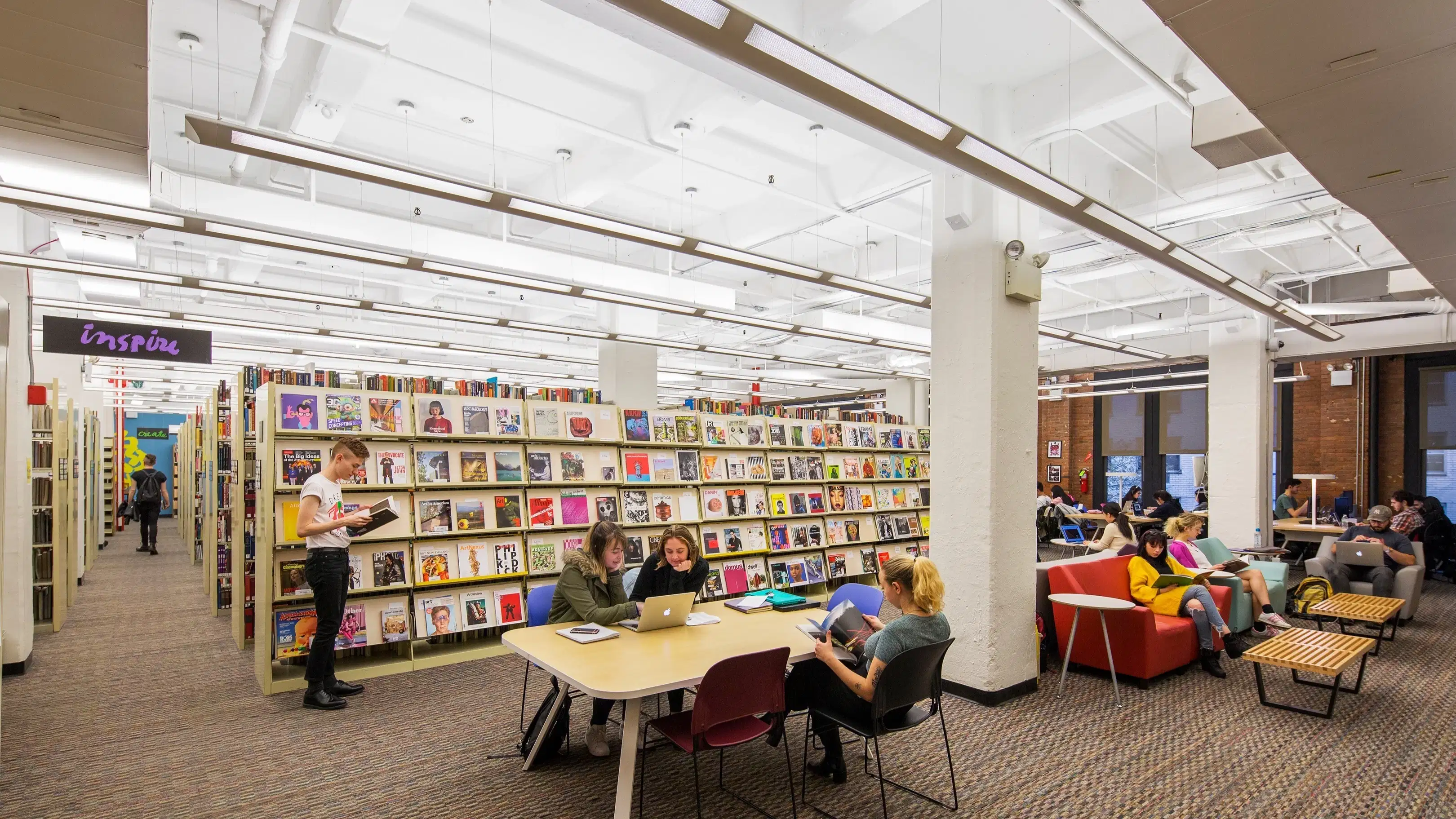 interior view of a library with stacks, study tables, couches and students working with one another