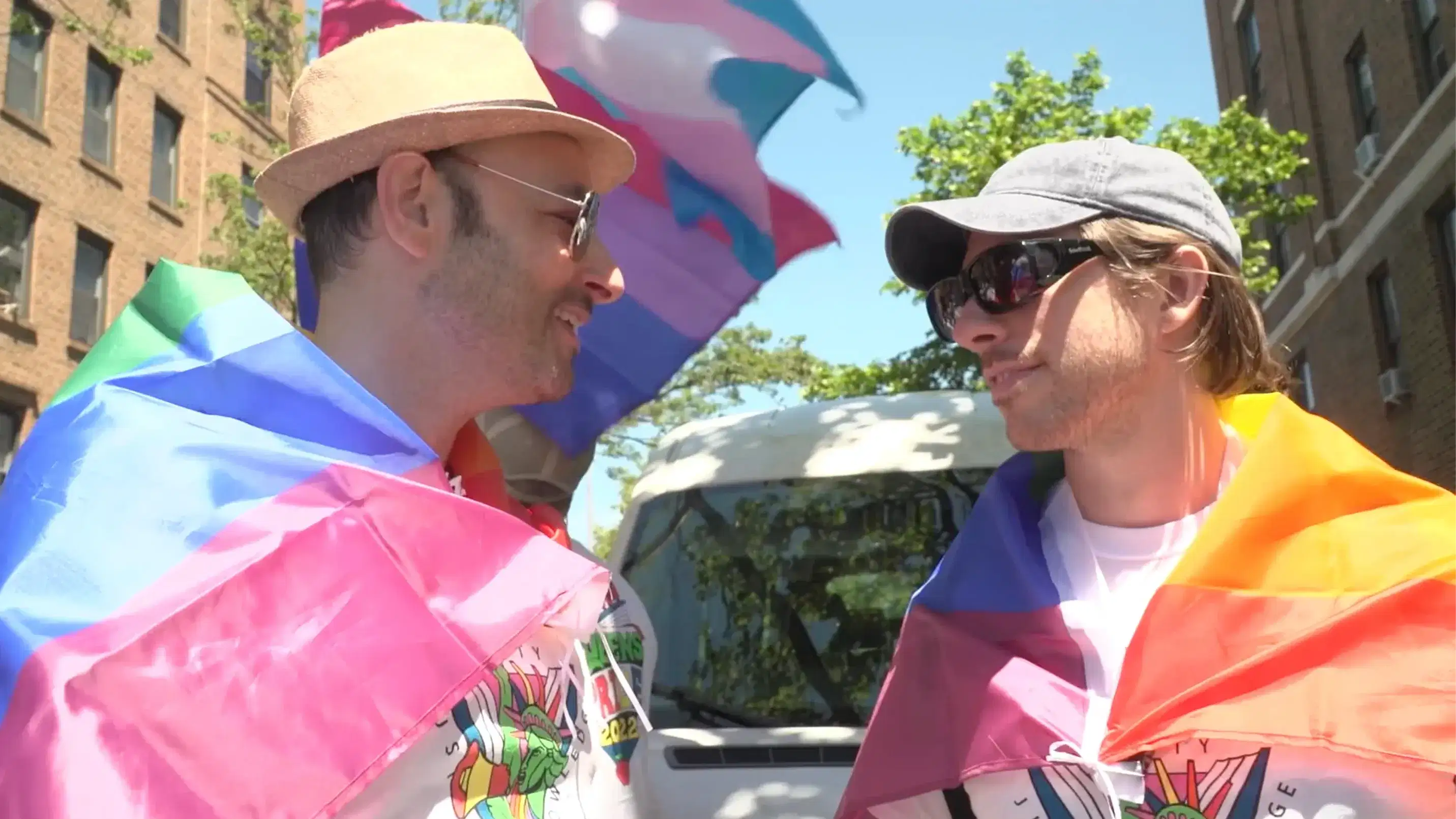 Two men wrapped in pride flags under the sun facing each other 