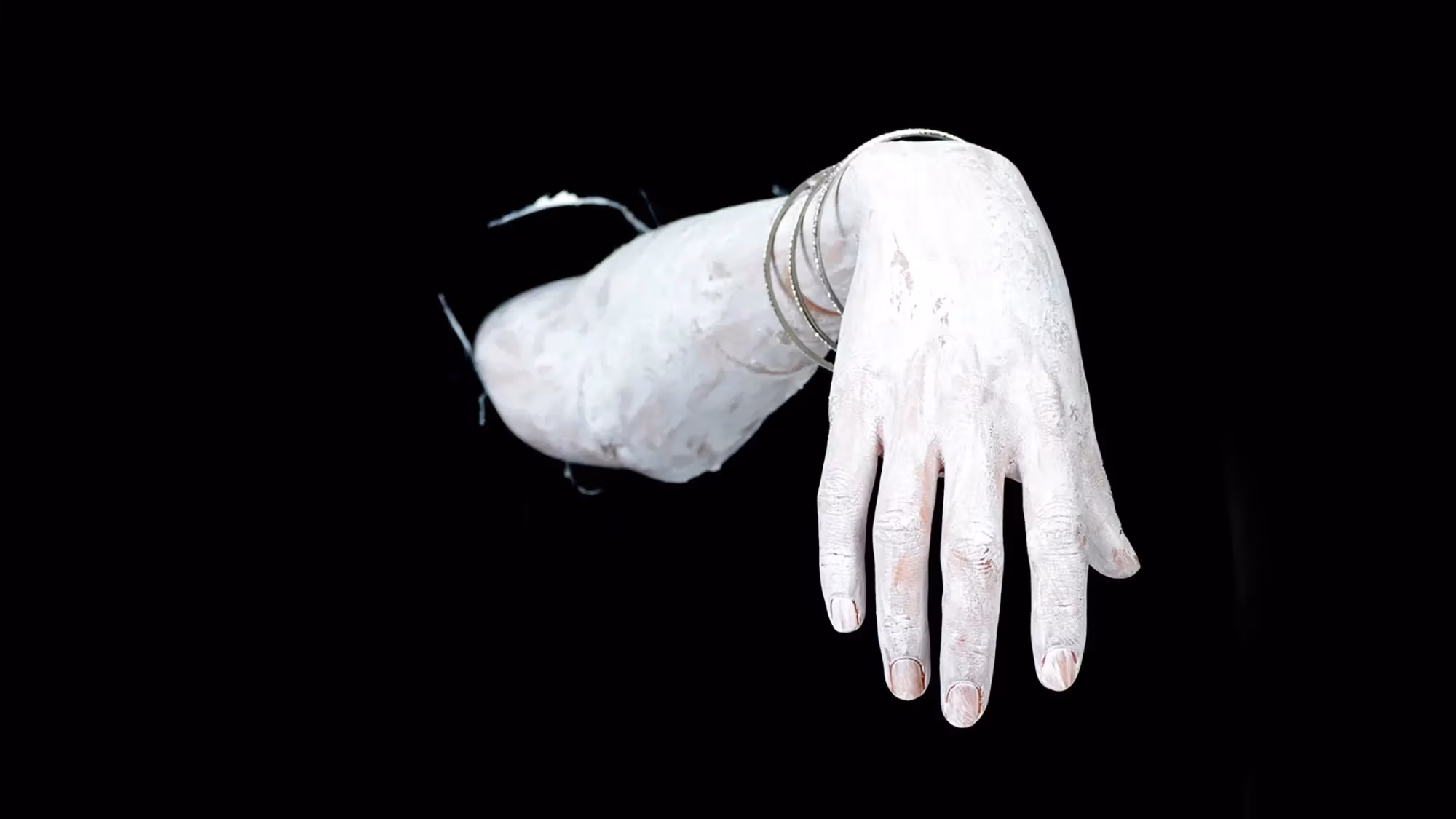 A hand and forearm emerging from darkness, covered with white paint.