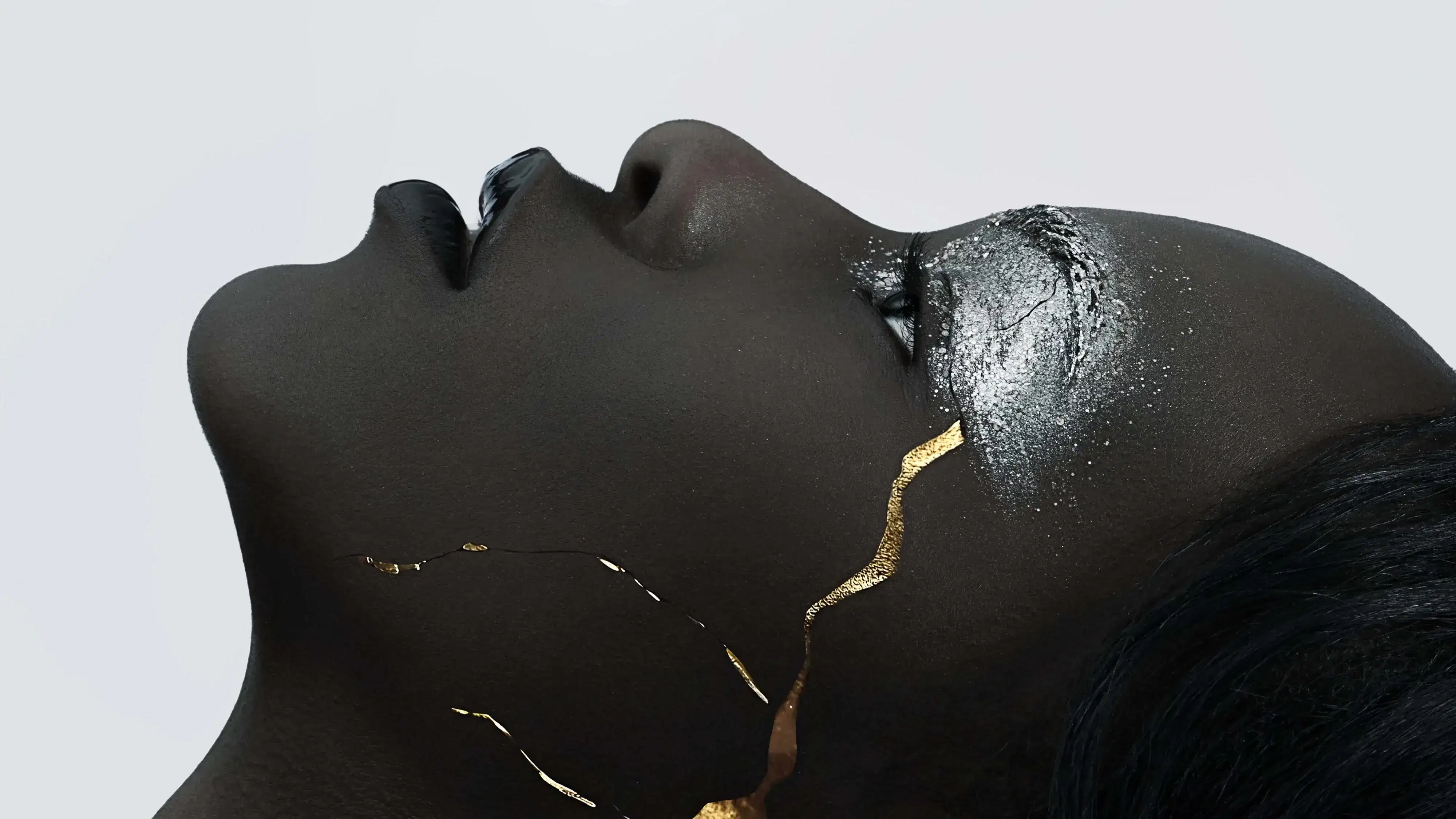A close-up profile view of an African woman staring towards the top of the frame. She's wearing silver glittery eyeshadow. A gold crack goes up the side of her cheek.