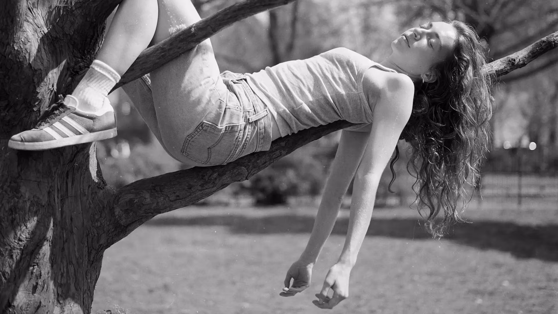 Black and white photograph of a girl resting on a tree branch.