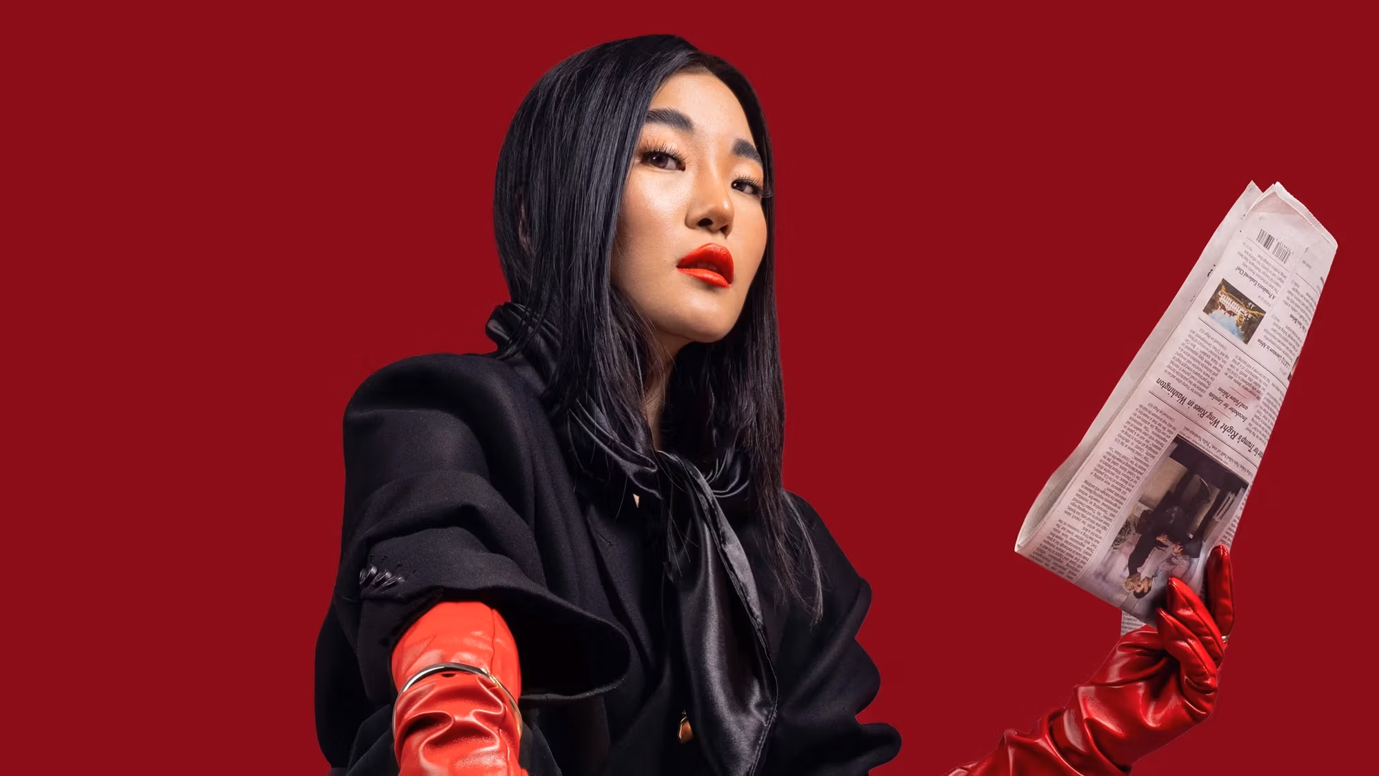 In front of the strong red solid background, the female model is wearing a matching black suit (blazer and dress pants) with black point toe heels. There are newspapers everywhere on the ground and the model is standing on it to symbolize the desire of wanting to become an important figure in the fashion (publication) industry.