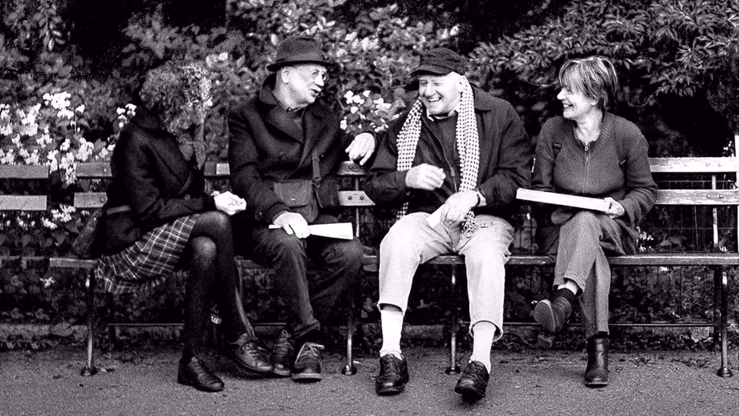 Four friends are sitting shoulder to shoulder in the park talking.