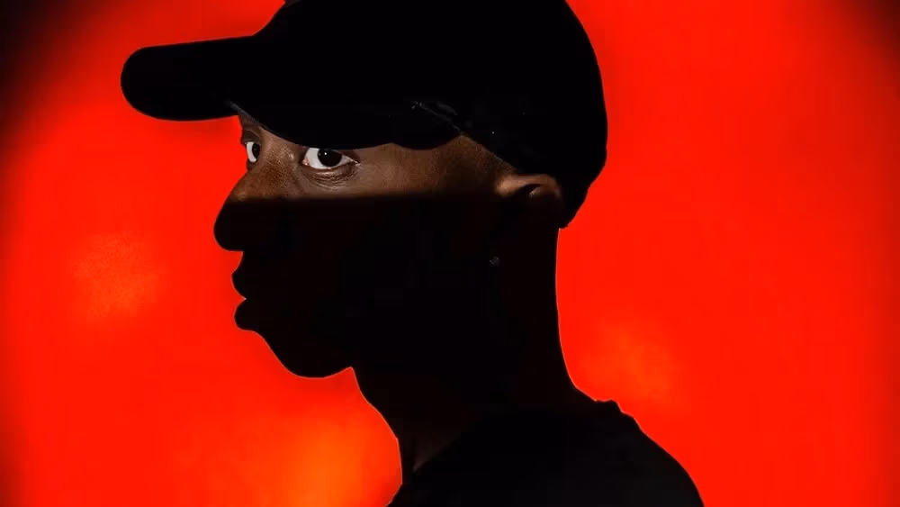 Red backlit circular background, partially silhouetted man with a target on his back
