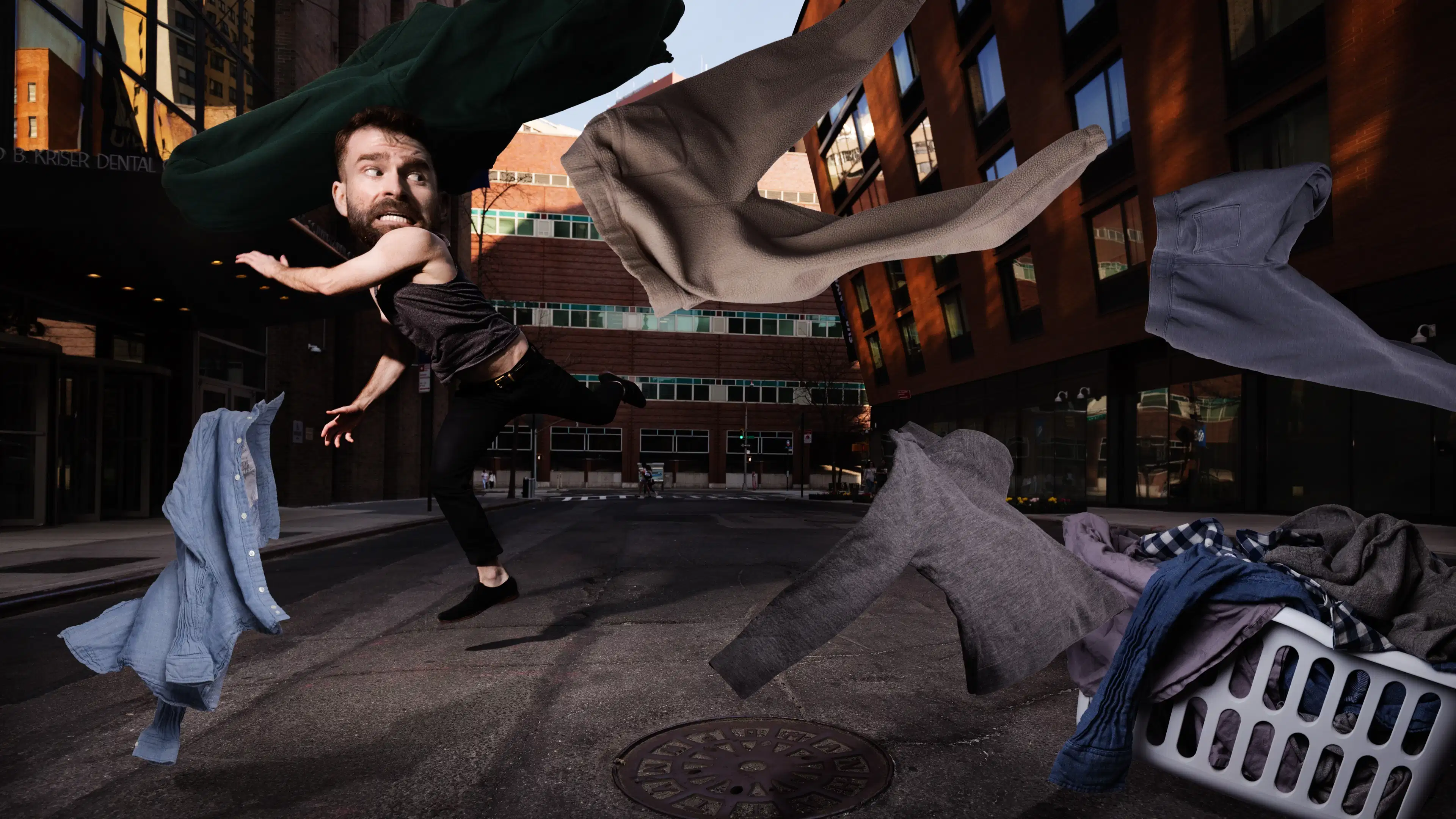 A composite photograph of a man running on an empty city street. His head has been enlarged and he is looking over his shoulder with a frightened expression. Around him is a basket of laundry with clothes flying through the air.