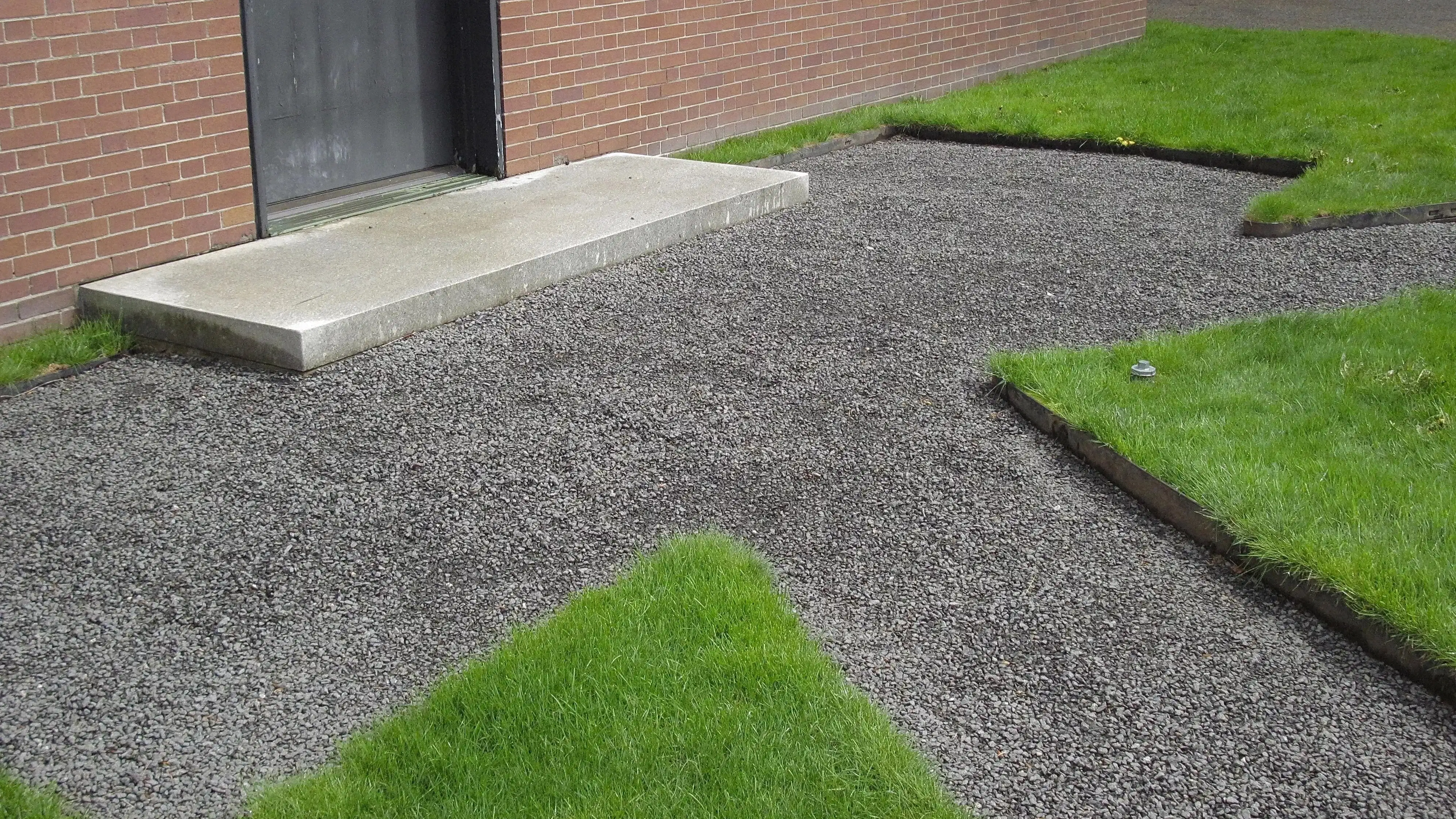 A gravel walkway leading to a door and surrounded by green grass.