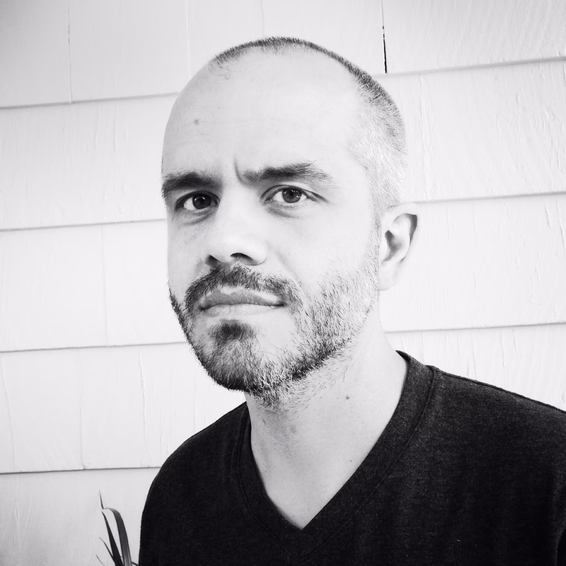 Head shot of Adam Bell, man with short dark hair and closely-cropped beard in black v-neck t-shirt