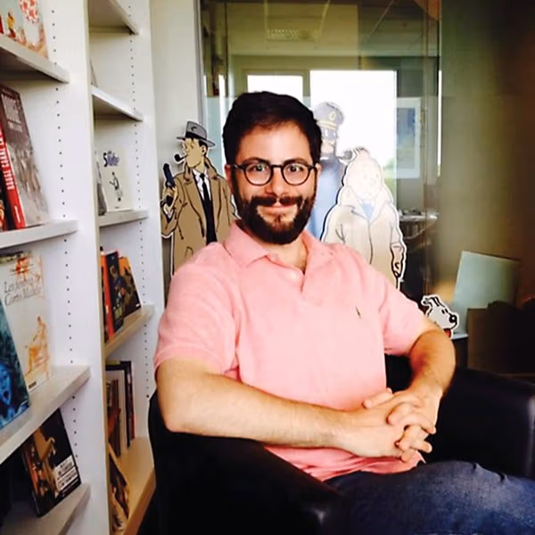 A portrait of Bill Kartalopoulos in an office surrounded by cartoon cut-outs