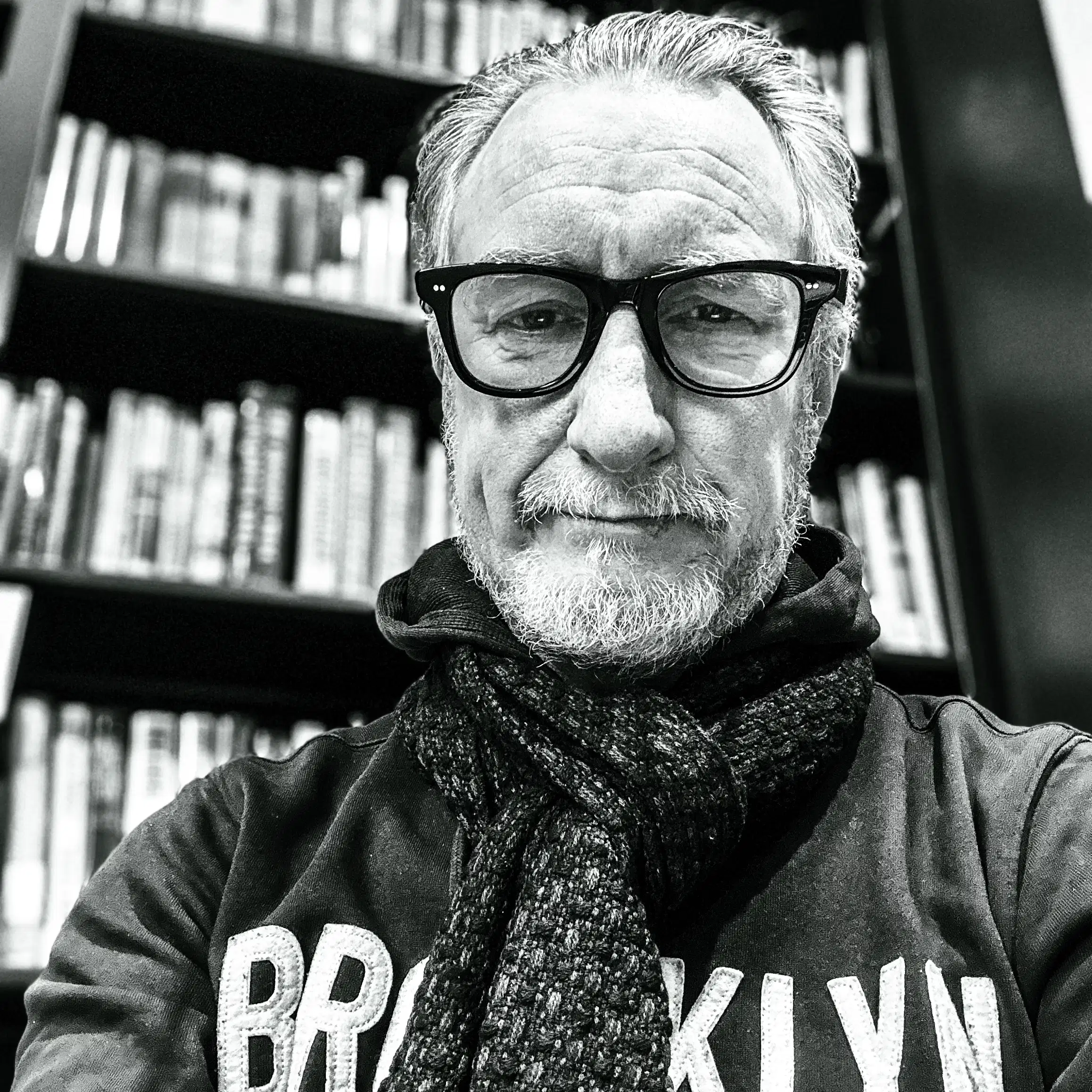 Photo of man with short beard, black-rimmed glasses wearing a Brooklyn hoodie and a scarf.