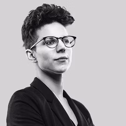 a person with glasses and a dark suit looks off camera