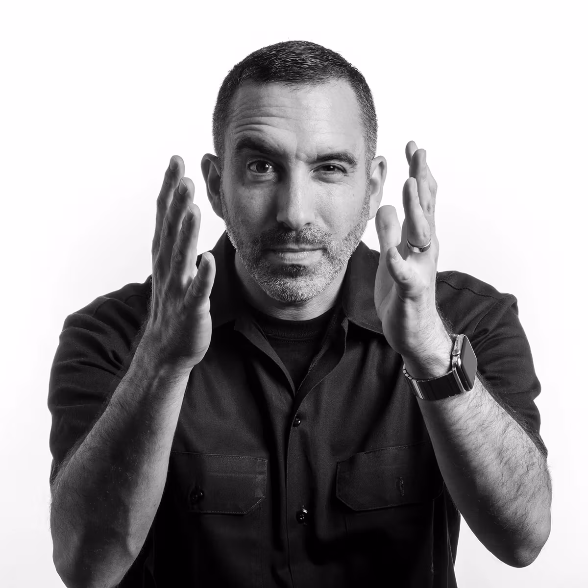 Black and white portrait of a middle-aged man with short dark hair and facial stubble, wearing a dark button-up shirt.
