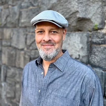 Portrait of a person with a blue shirt and cap smiling into the camera