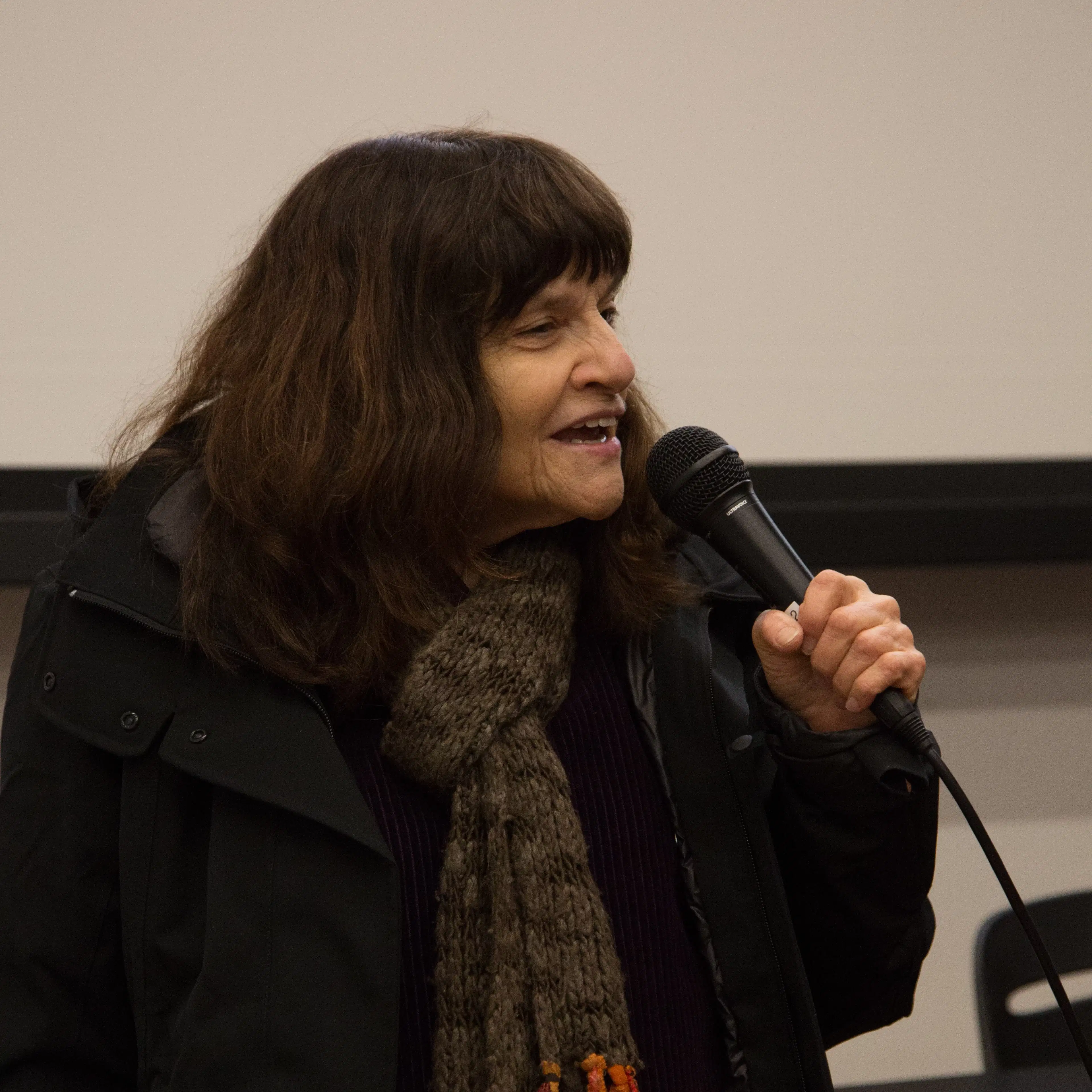 Image of a woman speaking into a microphone wearing a scarf.