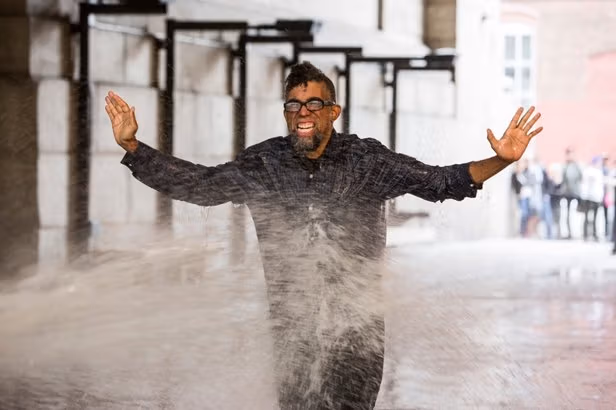 A man with glasses getting sprayed with water.