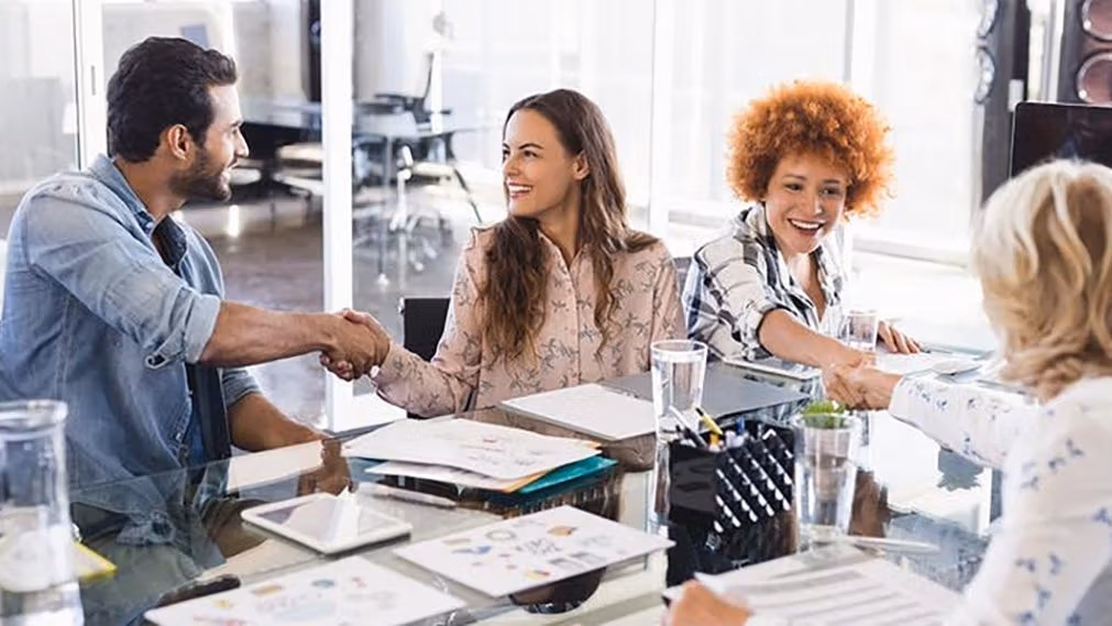 group of people at a conference table shaking hands hello happily