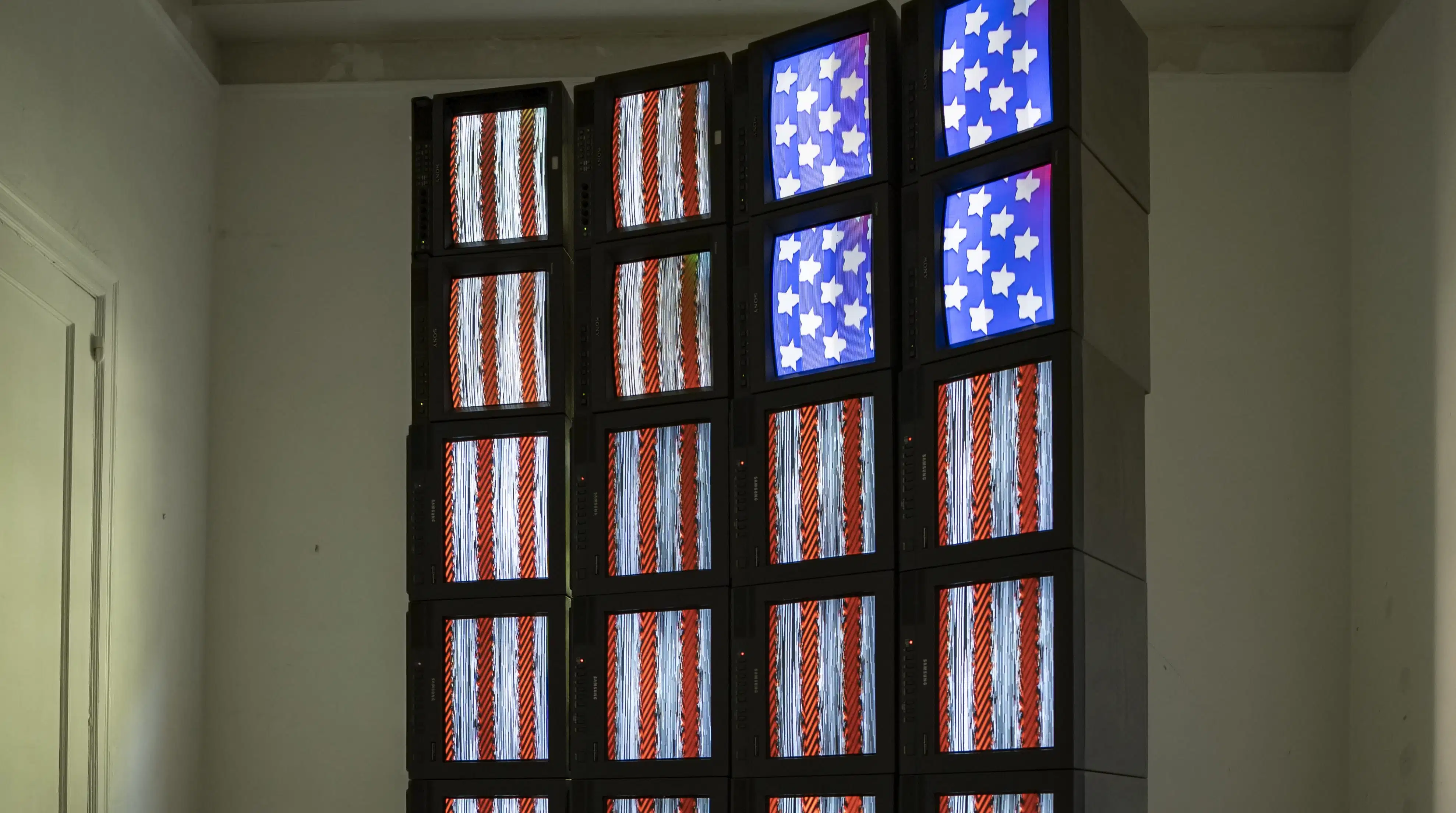 Twenty-four screens, stacked in four columns, displaying one large stylized American flag when viewed at a distance.