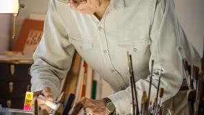 An old man bent over a desk gluing something.