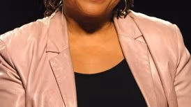 An African American in a tan blazer and white undershirt.