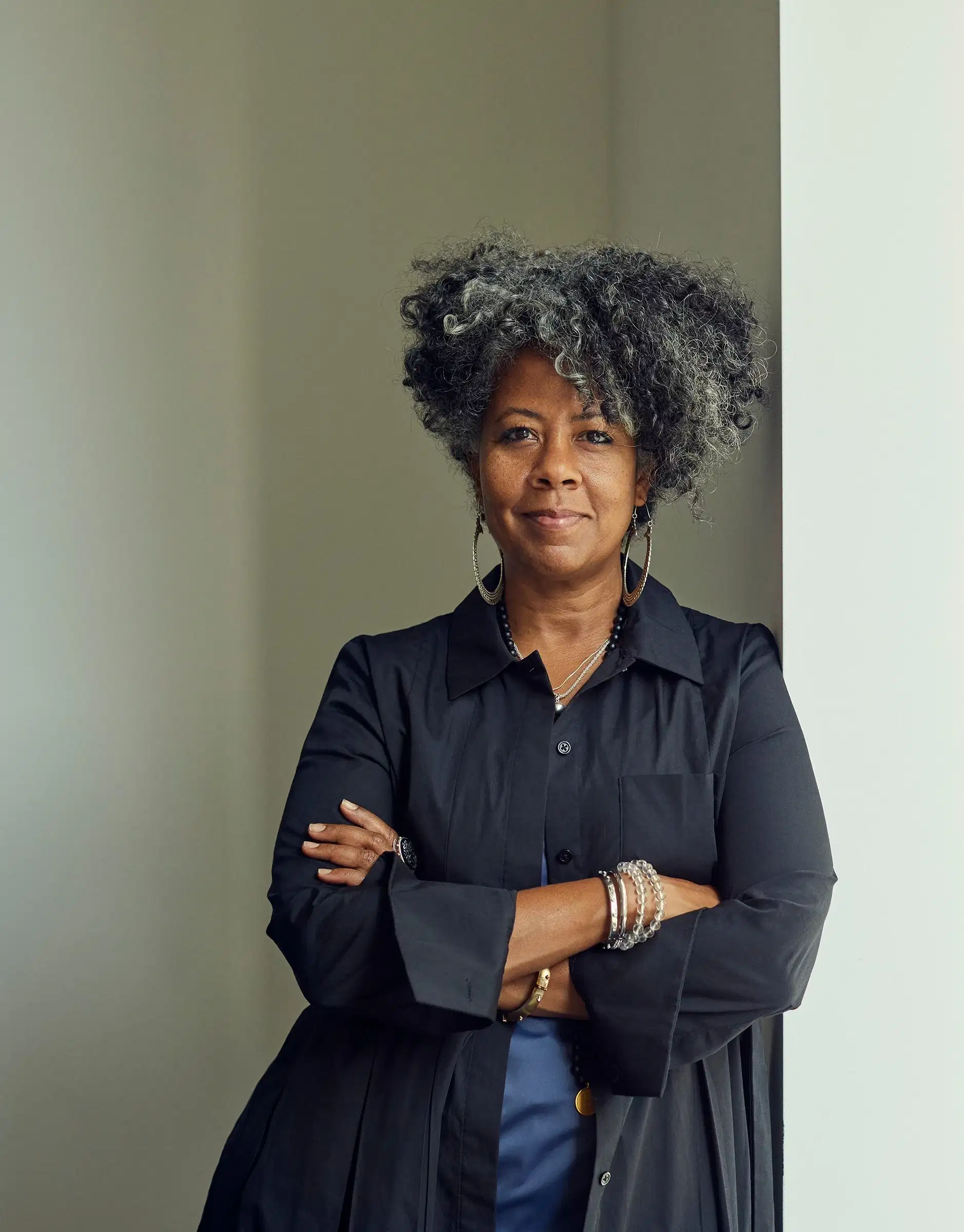 Portrait of the artist Torkwase Dyson smiling and leaning against a wall with arms crossed.