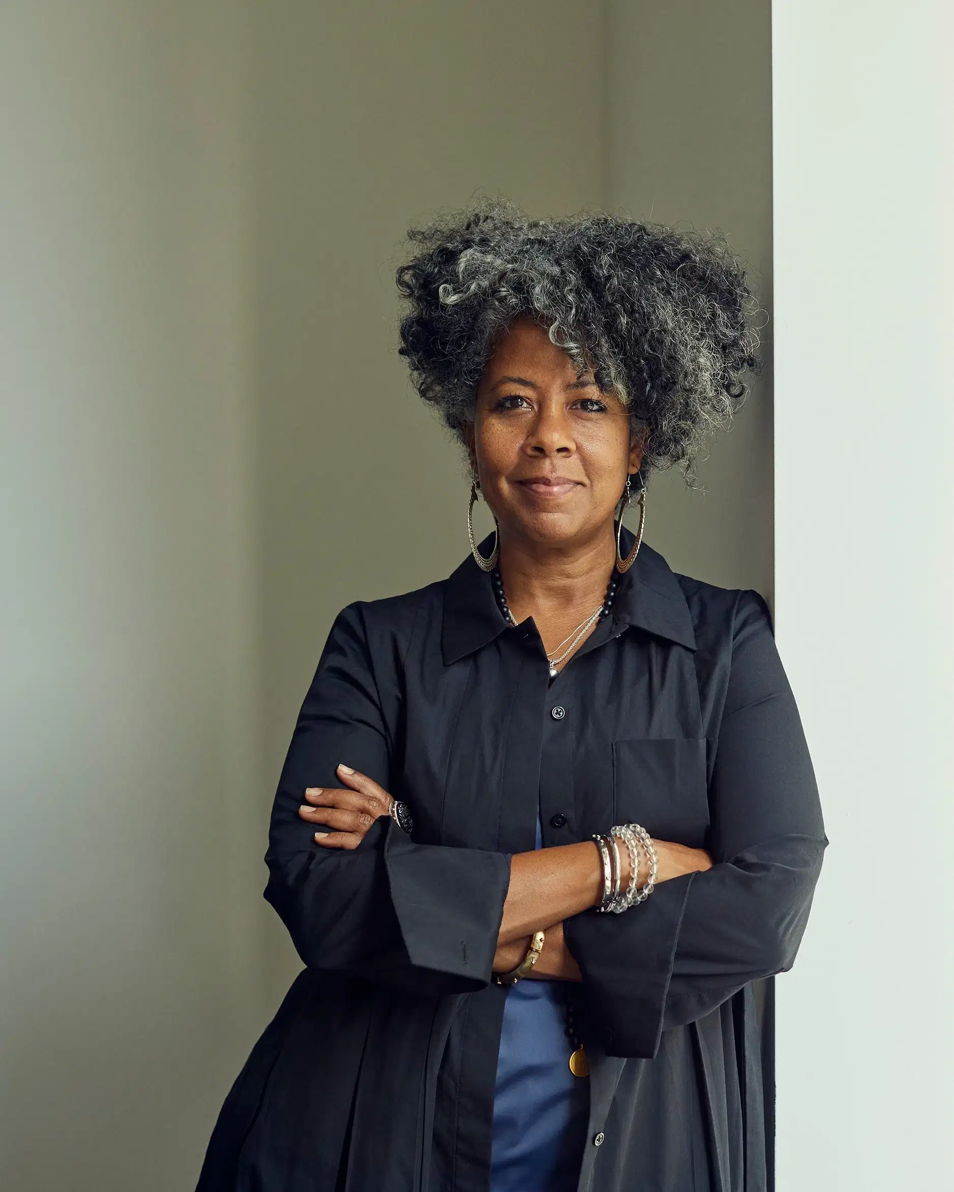 Portrait of the artist Torkwase Dyson smiling and leaning against a wall with arms crossed.