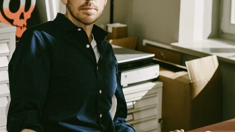 An artist looking into the camera, there is a drawing in front of him