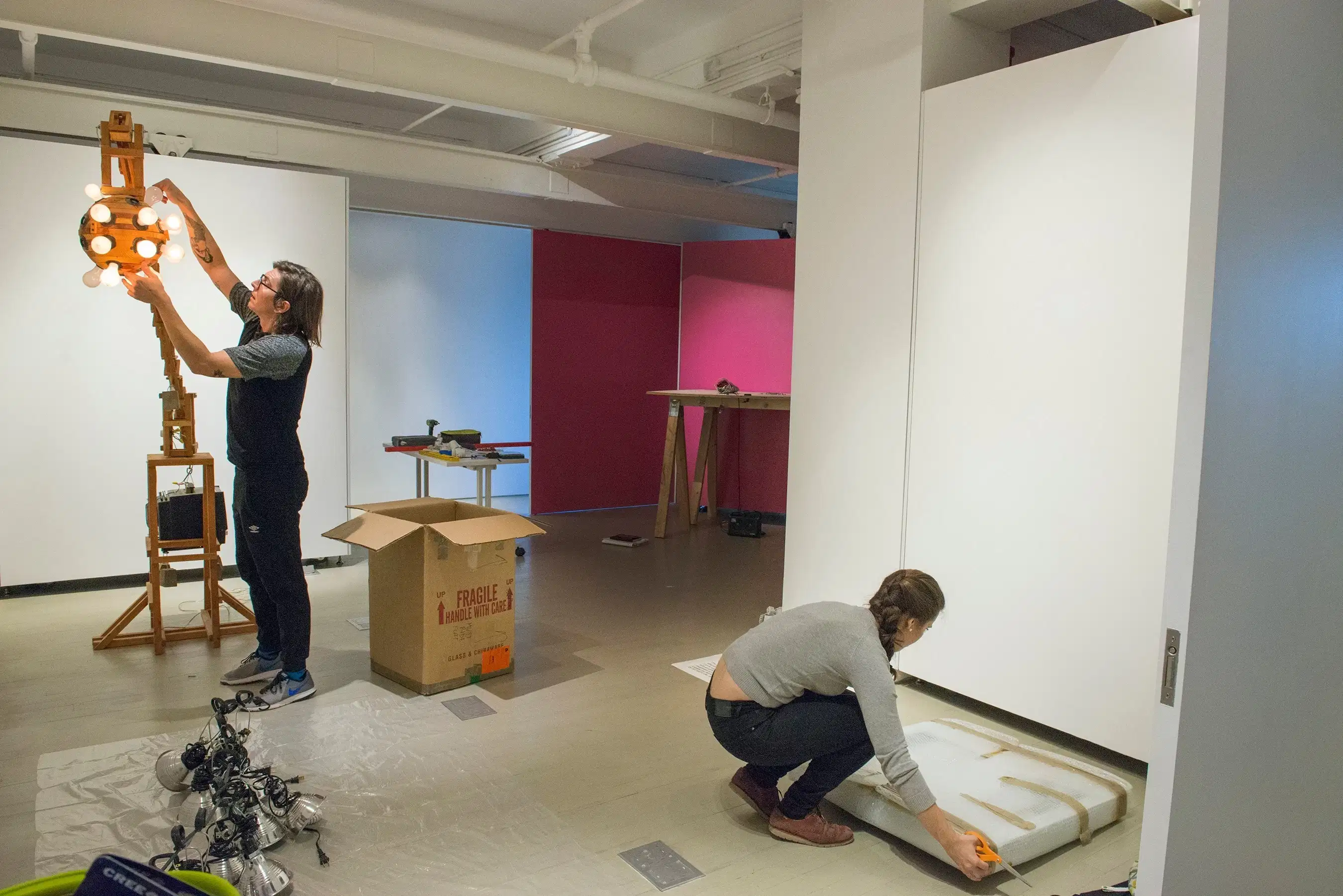 Two students unpacking and hanging artwork in a gallery space 