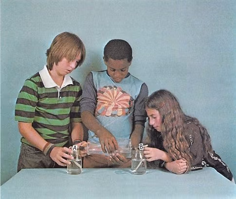 Three young teenagers are conducting a science experiment featuring two beakers filled with water.