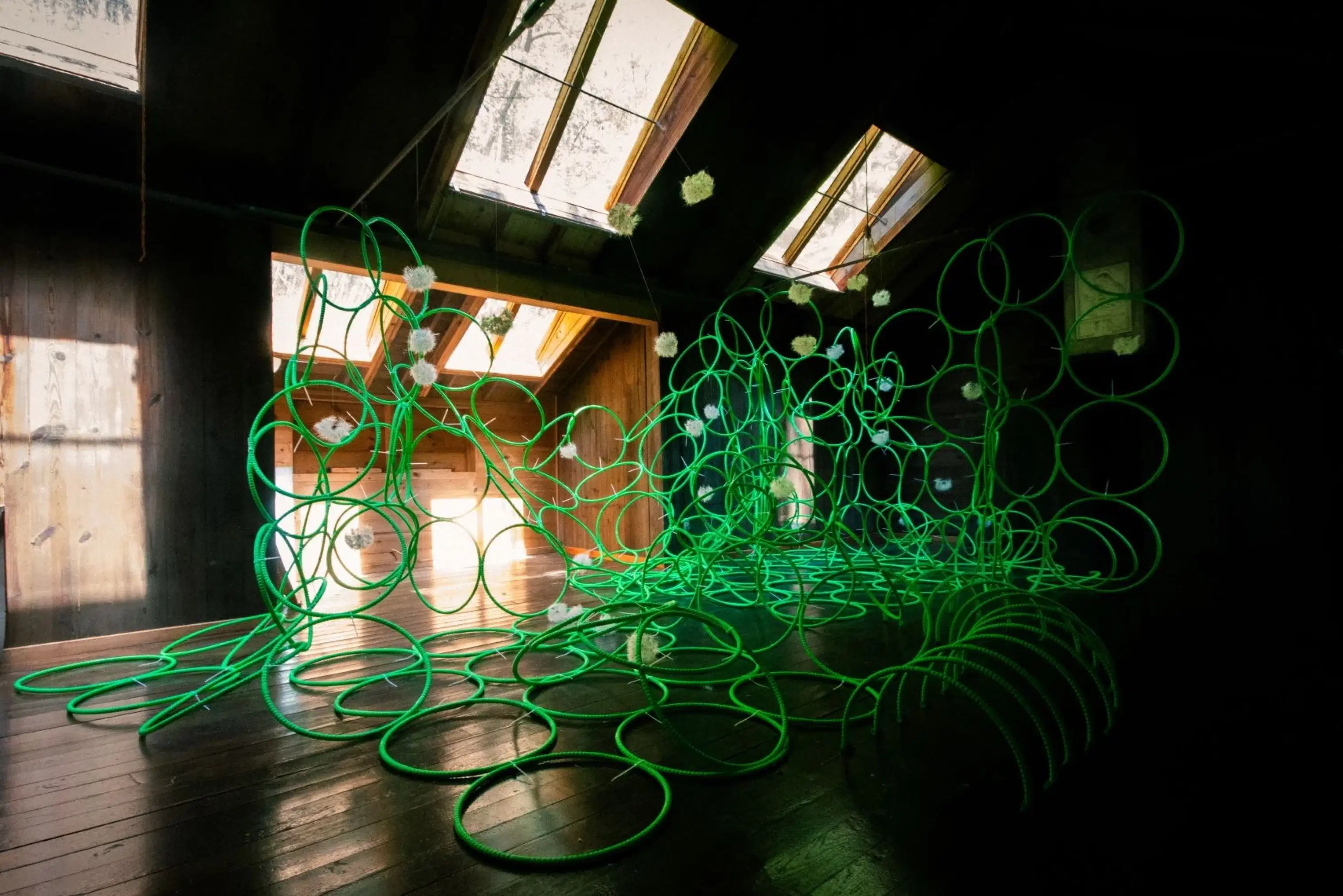 photograph of green hula-hoops in a sculptural assemblage in a dark barn with sunlight coming in through windows