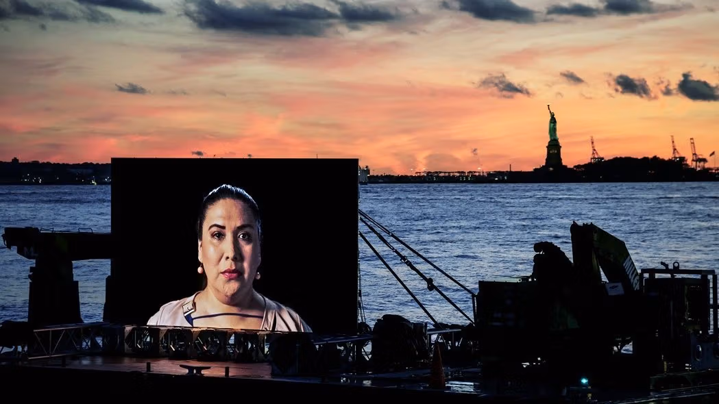 A large portrait of a woman with the sunset, water and Statue of Liberty in the background