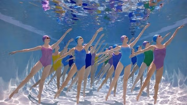 Female synchronized swim team posing under water.
