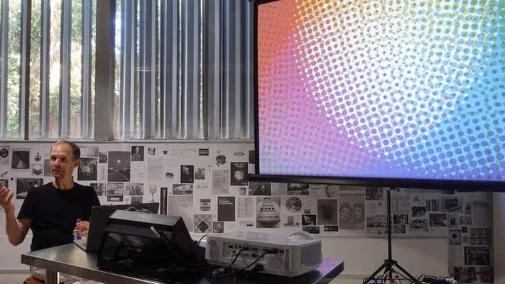 An image of a man taking next to a large projector screen