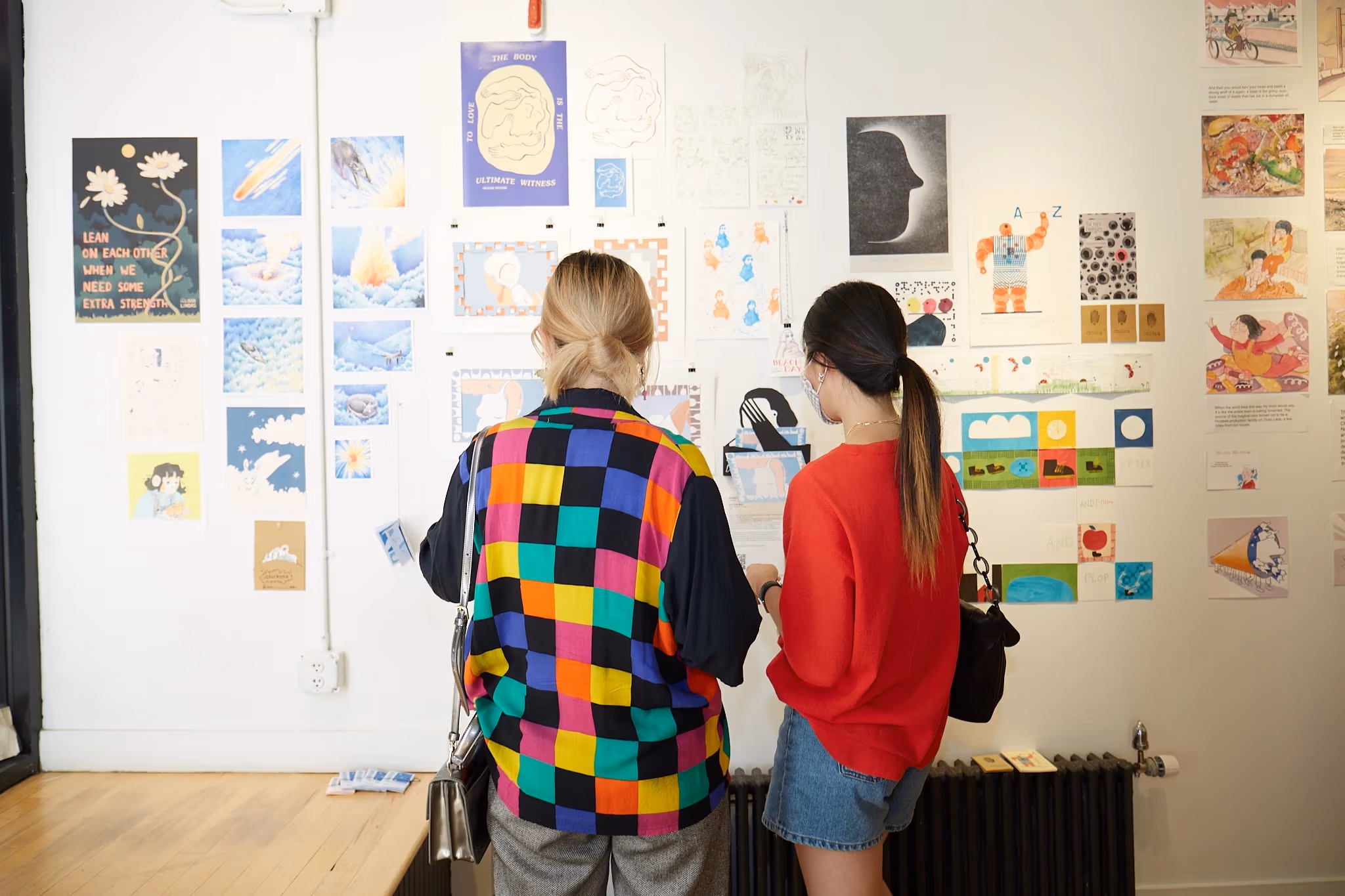 Two people looking at a wall of illustrations