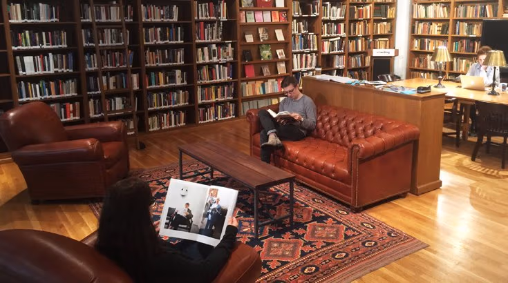 Three people reading or working in a room filled with books.